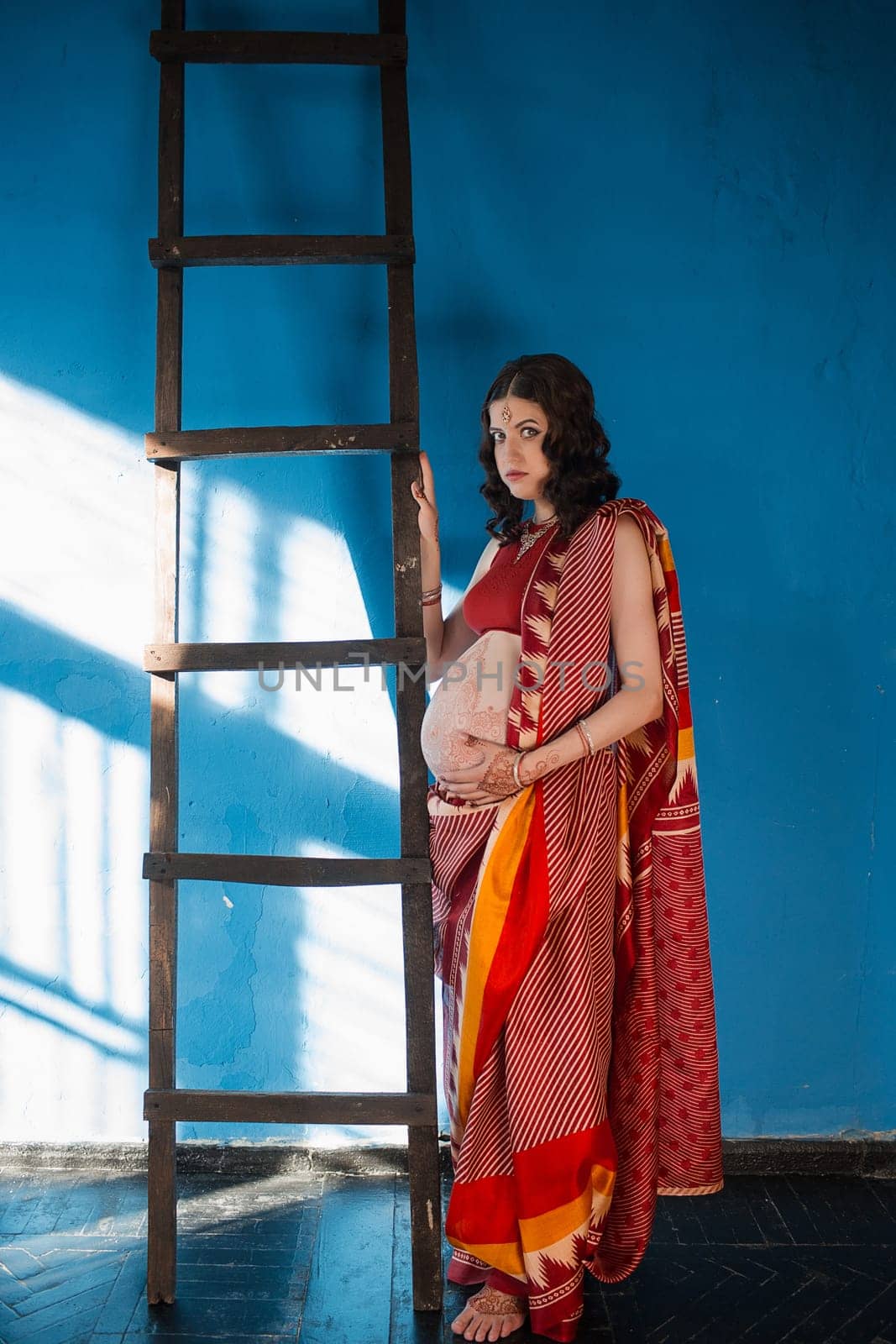 Indian picture on woman hands and pregnant belly with henna tattoo on blue wall background