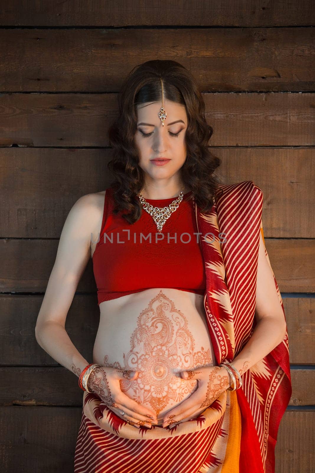 Indian picture on woman hands and pregnant belly with henna tattoo on wooden wall background
