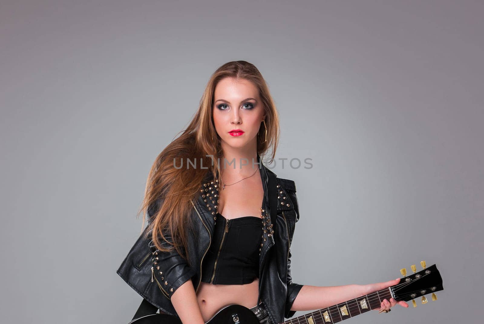 Beautiful girl  with long hair playing guitar in rock style on a gray background