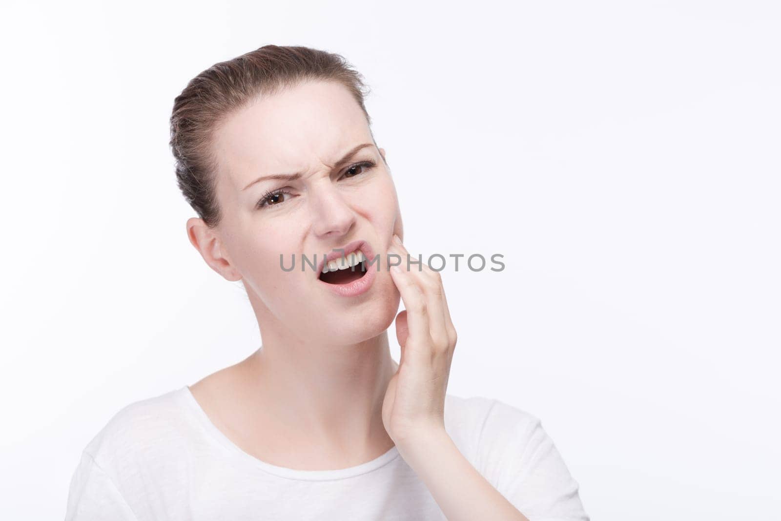 A young pretty woman in a white shirt holds her cheek from toothache