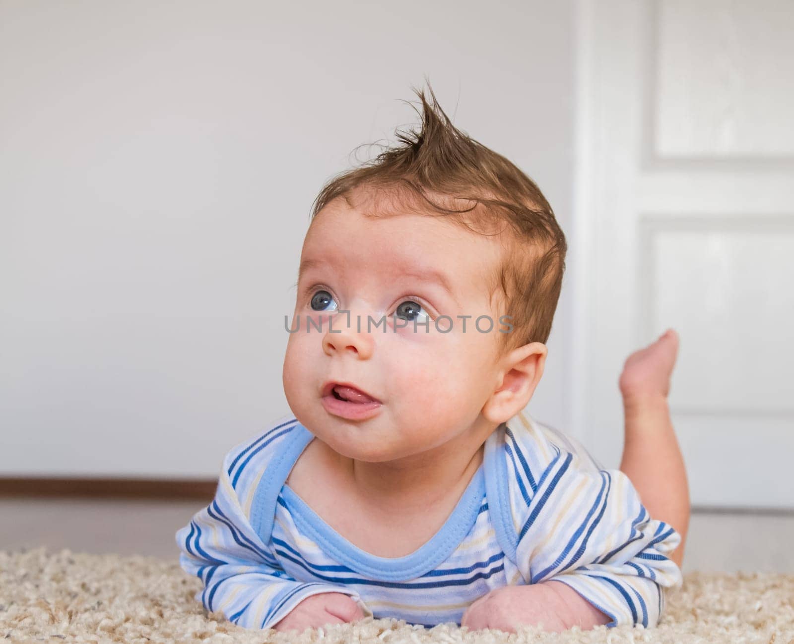 2 months old baby boy enjoying tummy time on the carpet at home.