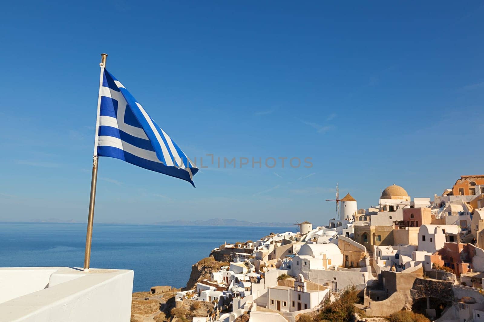 White villa houses and hotels with a perfect view of the volcano in the sea, Oia, Santorini Greek flag in front