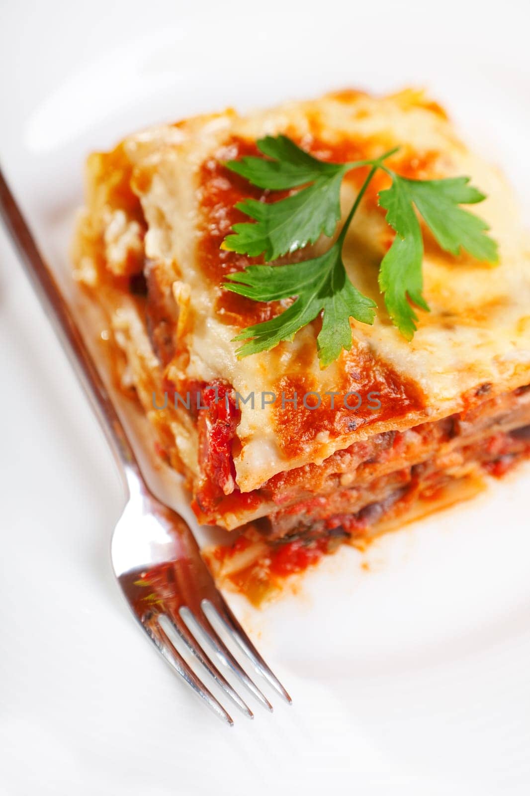 Lasagna bolognese served in a white plate with a fork