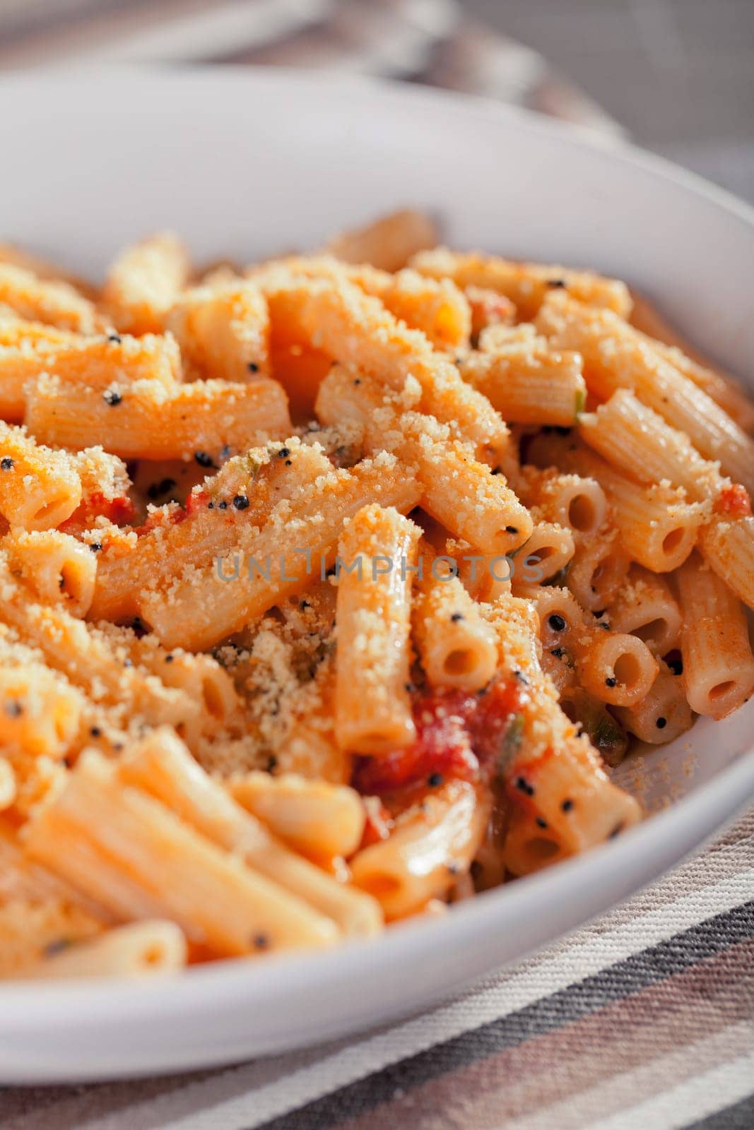 Penne with tomatos and parmesan cheese served in a white plate, close up