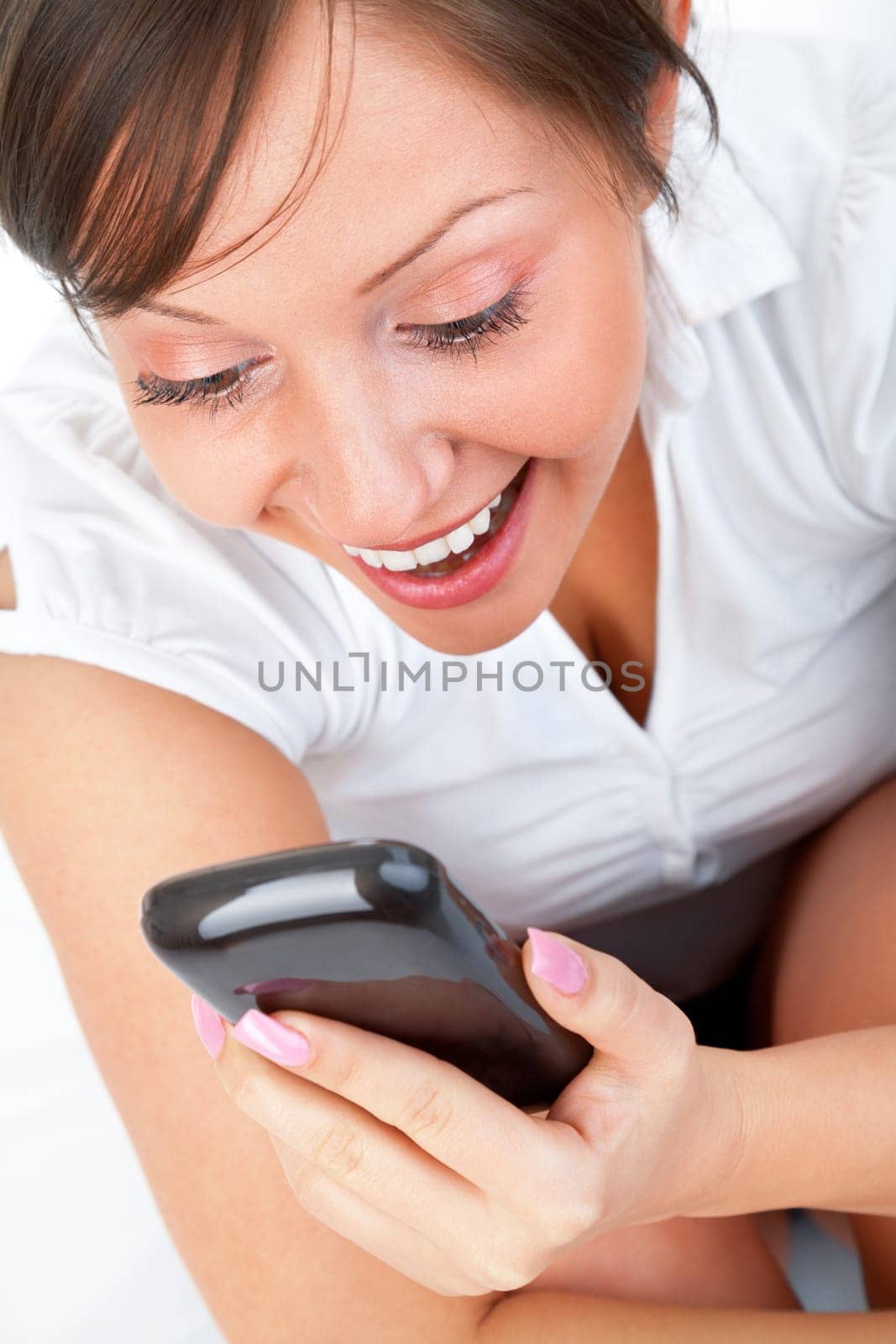 Young woman lying in bed and talking on the phone or reading sms isolated on white background