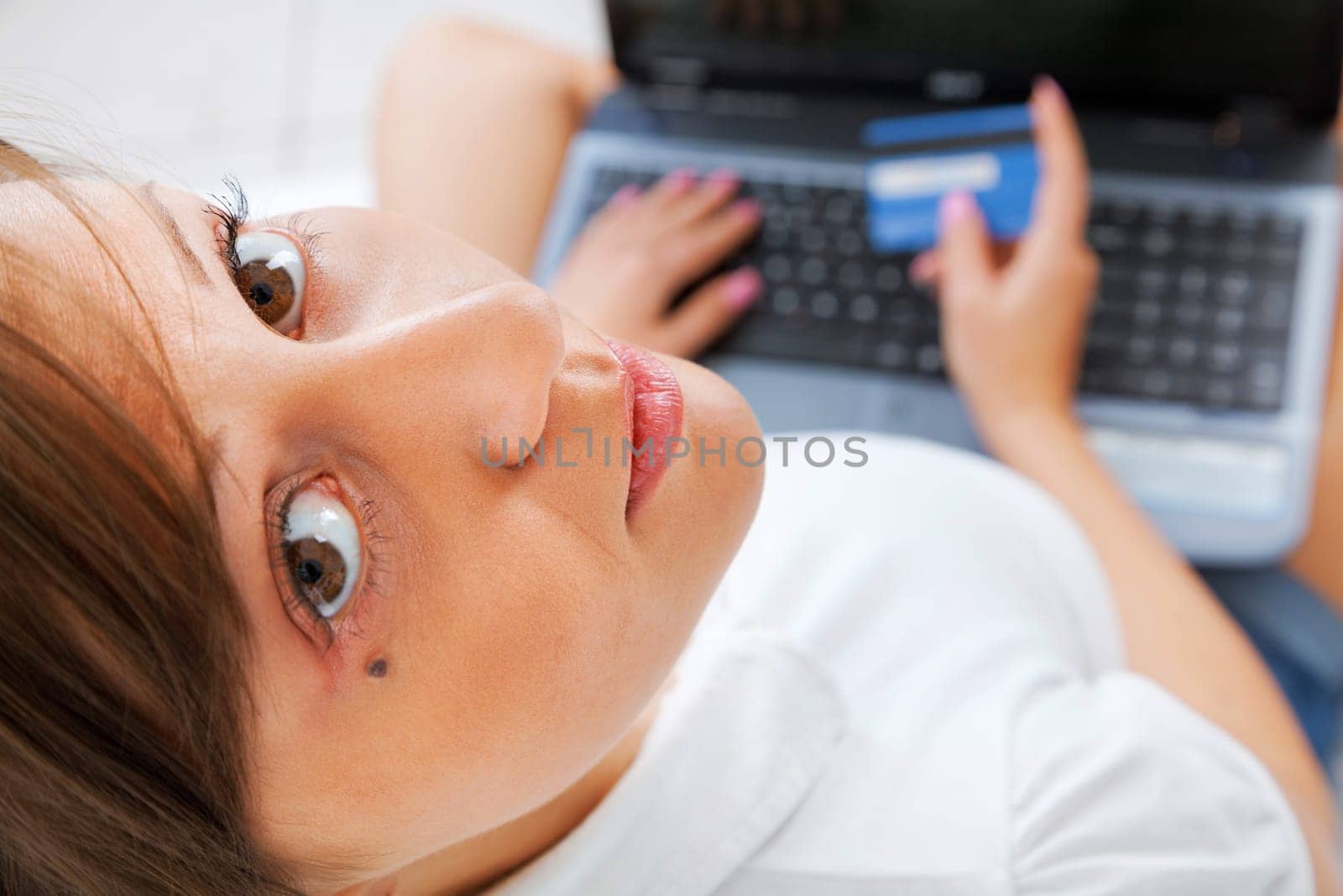 Young woman lying in bed and shopping online isolated on white background, shot from above
