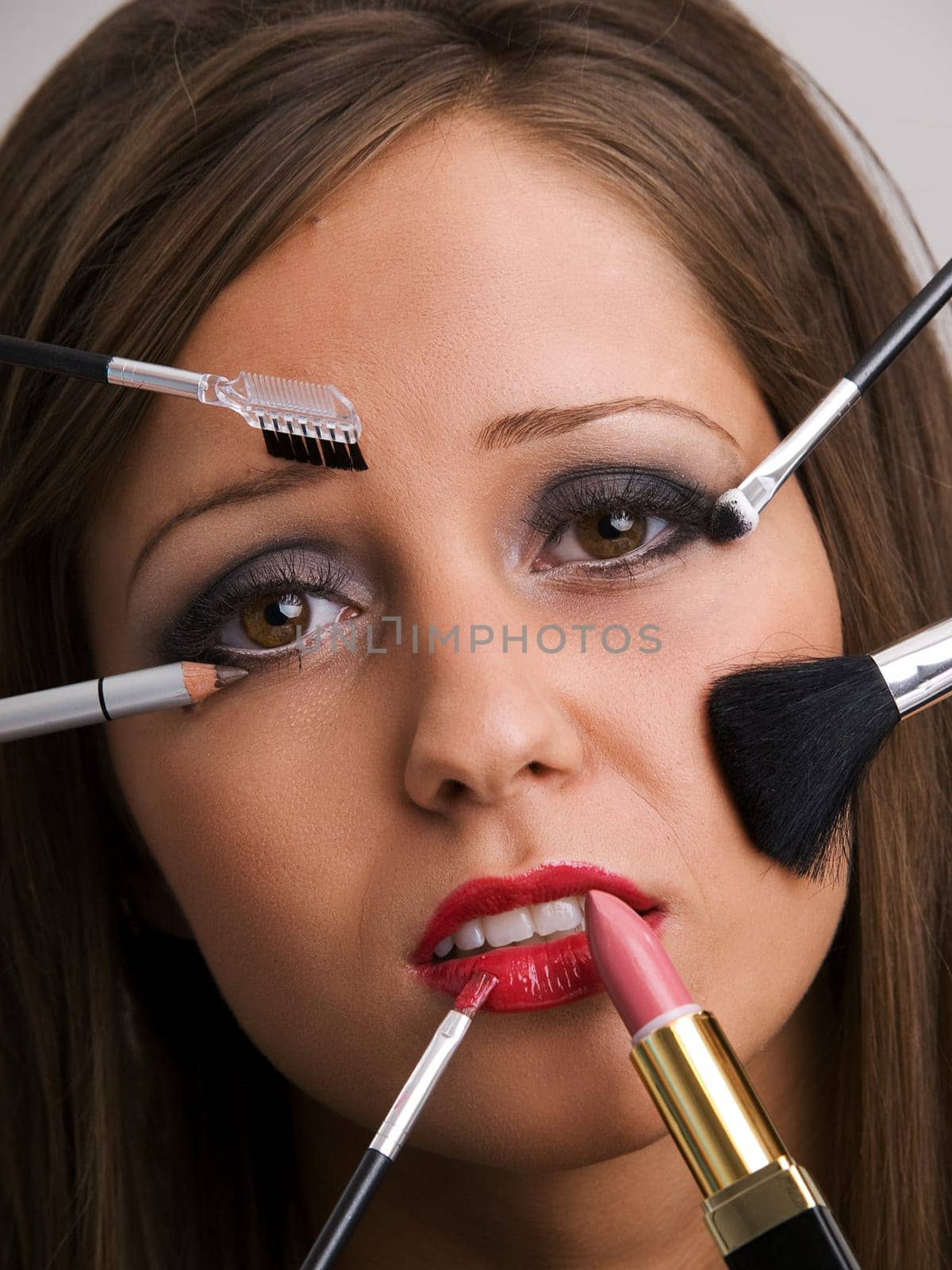 Close up of young woman face with all kinds of make up tools - brush, lipstick etc looking very bored or sad