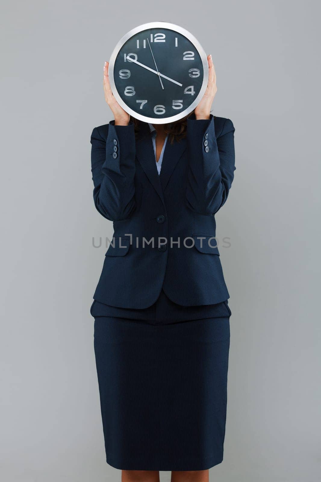 Businesswoman holdng a clock in front of her face isolated on gray background