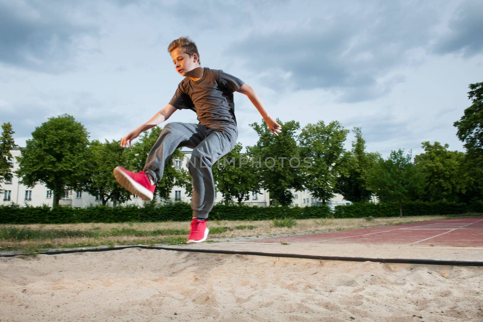 Side frontal full body view of a male young teenager frozen while jumping into a long jump pit