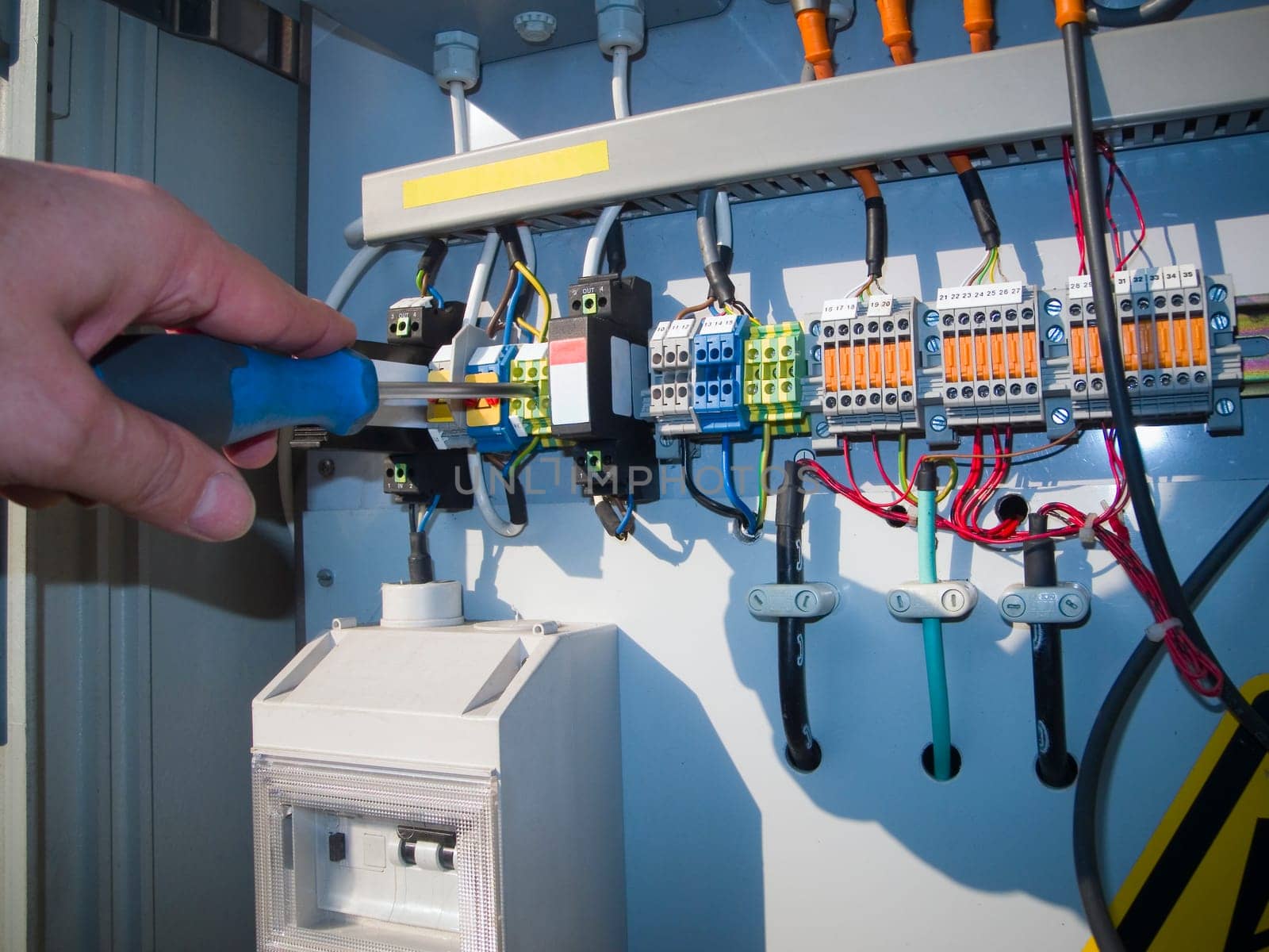 Hands of an electrician at an electrical switchgear cabinet.