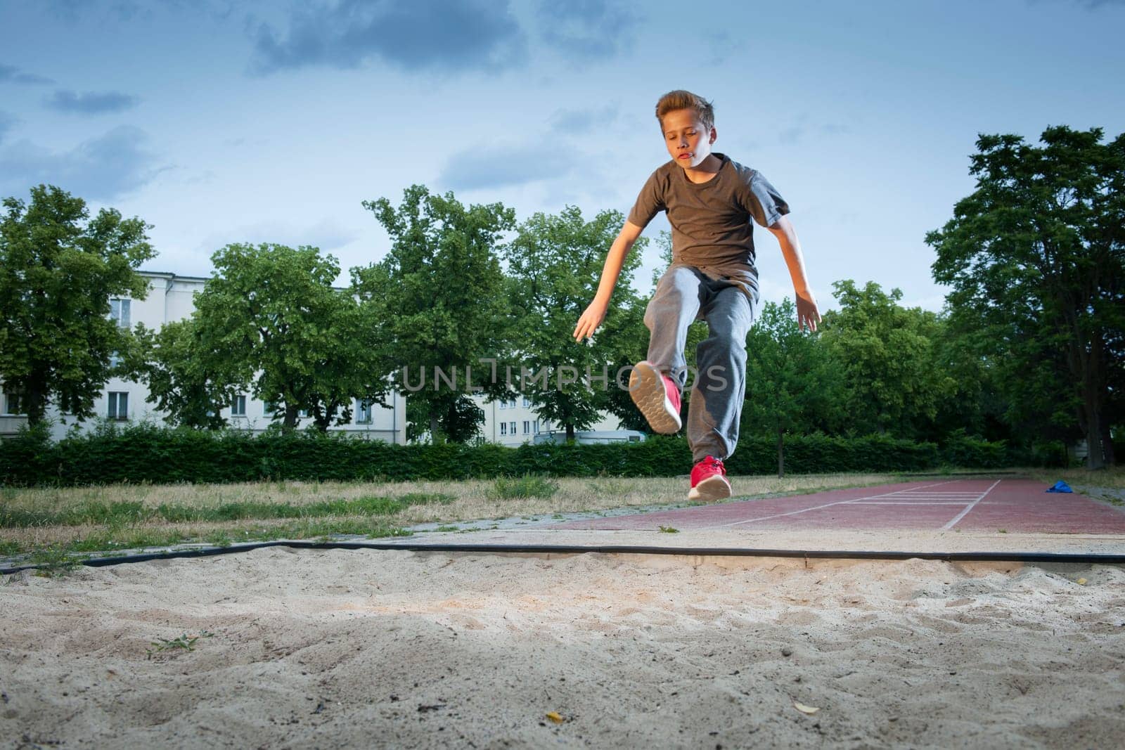 Side frontal full body view of a male young teenager frozen while jumping into a long jump pit