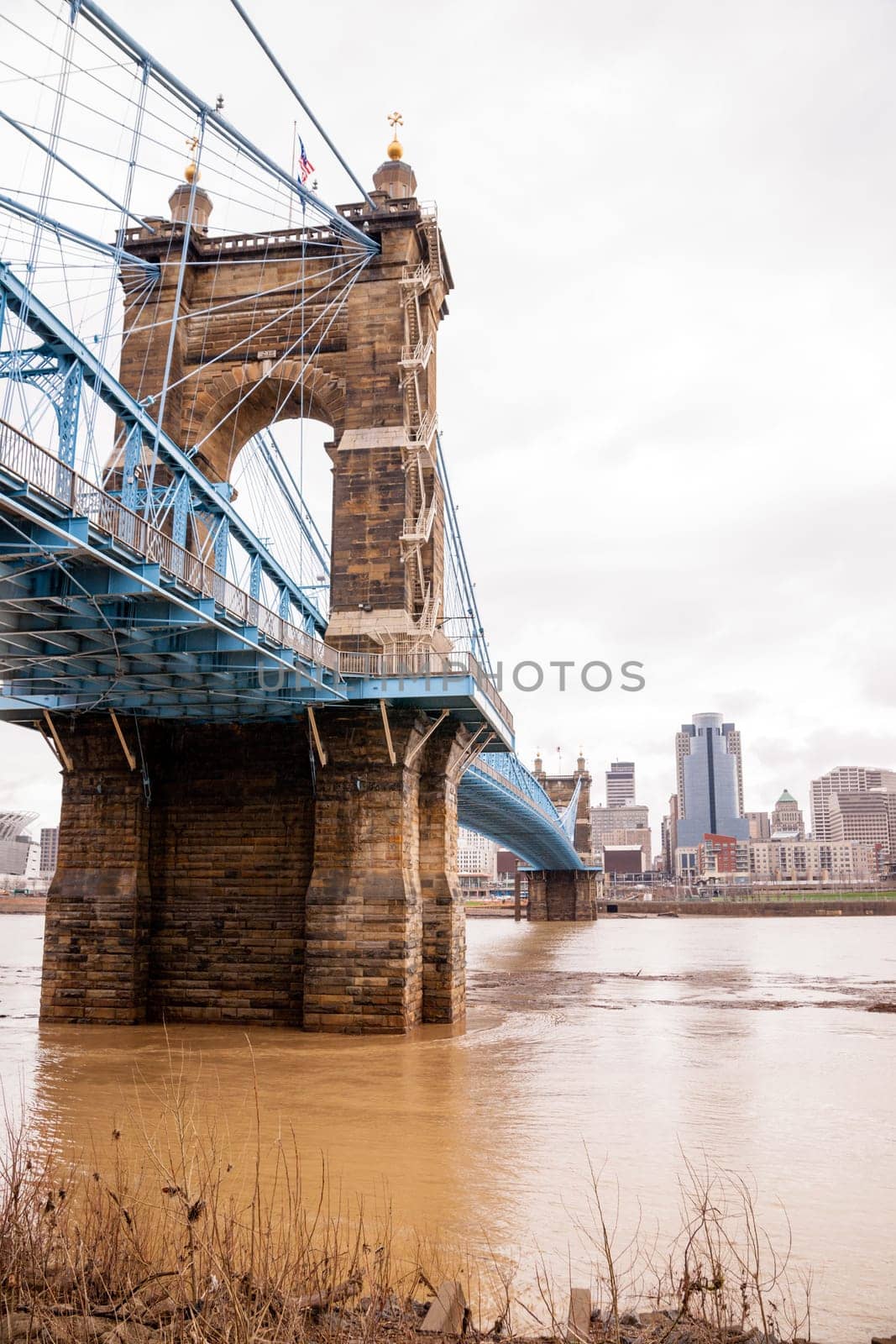The Ohio River is at flood stage as it passes underneath a historical suspension bridge