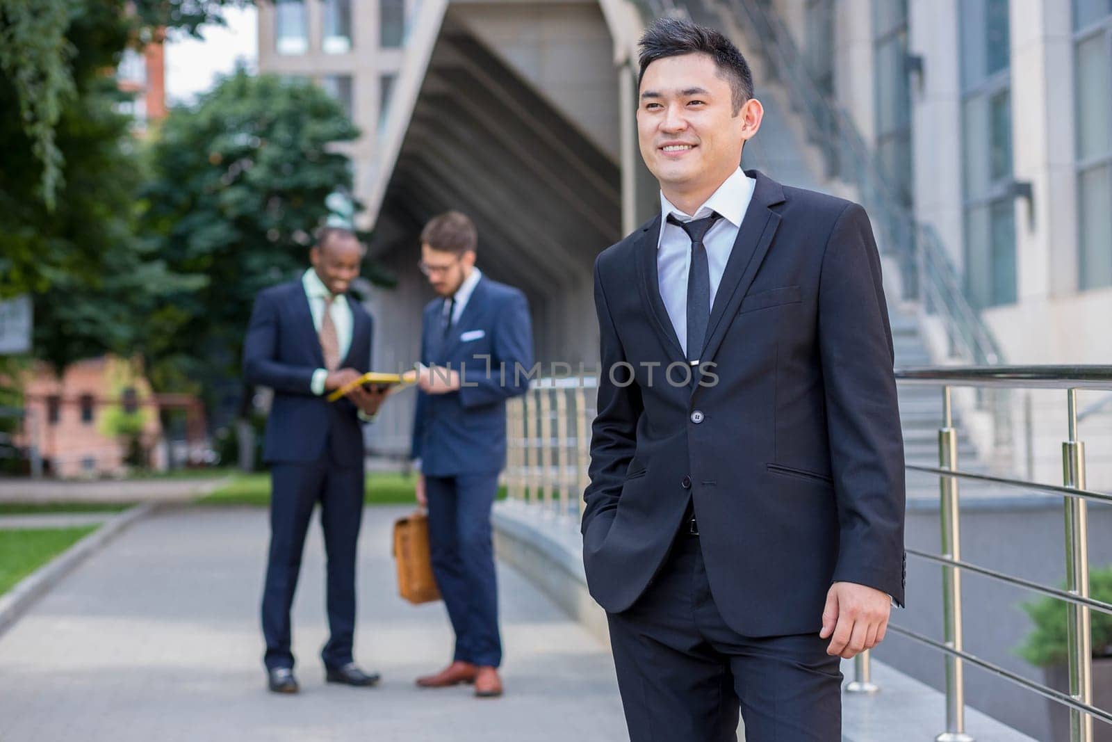 Portrait of multi ethnic business team. Three happy smiling men standing against the backdrop of the city.  The foreground of a Chinese  man