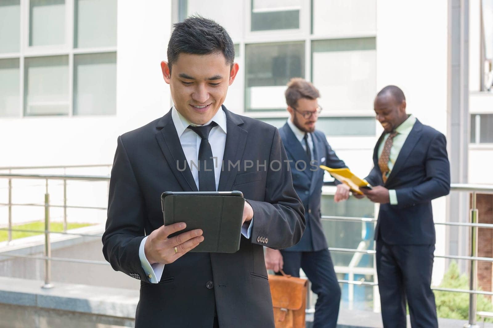 Portrait of multi ethnic business team. Three happy smiling men standing against the backdrop of the city.  The foreground of a Chinese  man  with laptop