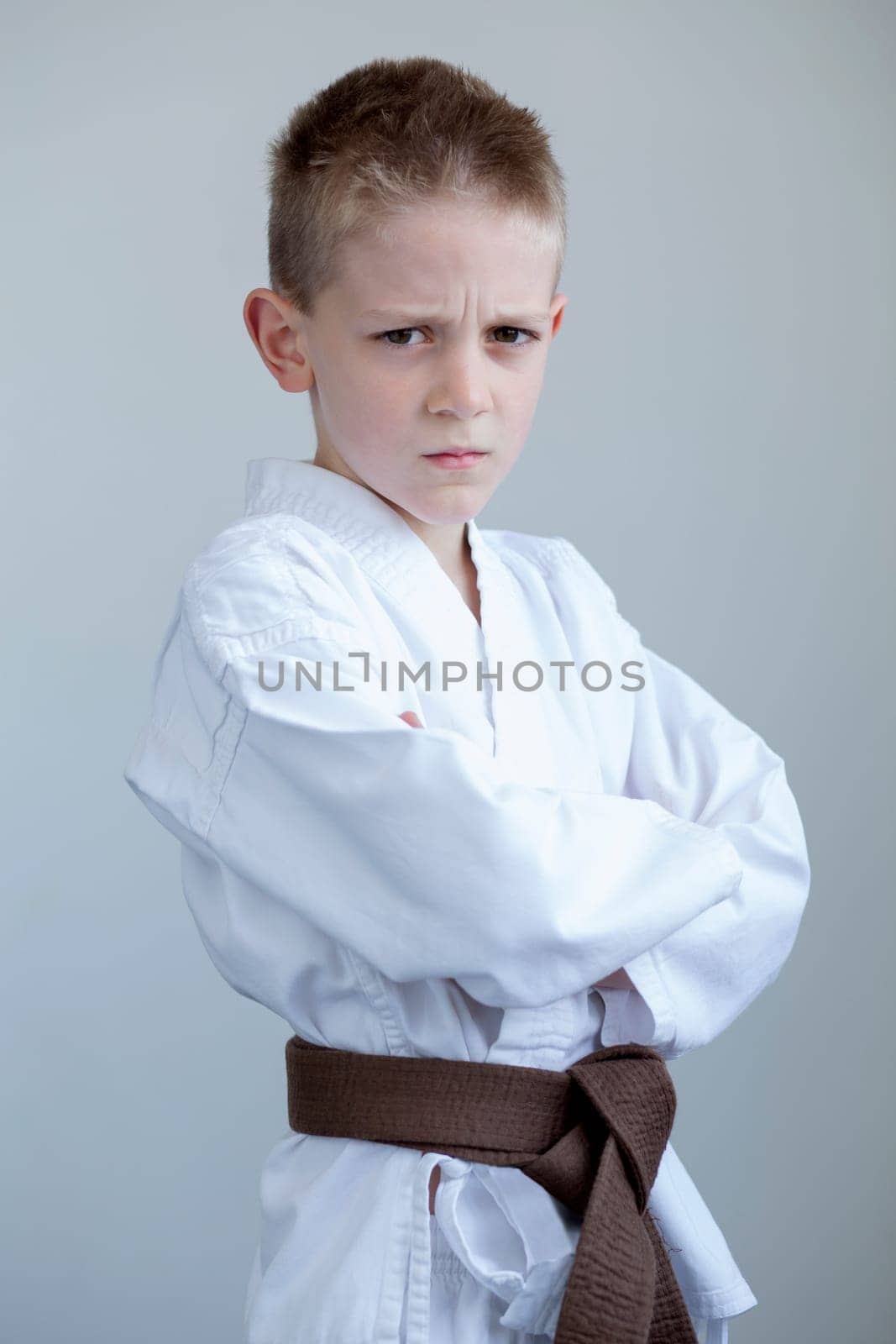 Young boy in karate clothing, posing with a tough expression on his face and his arms folded.