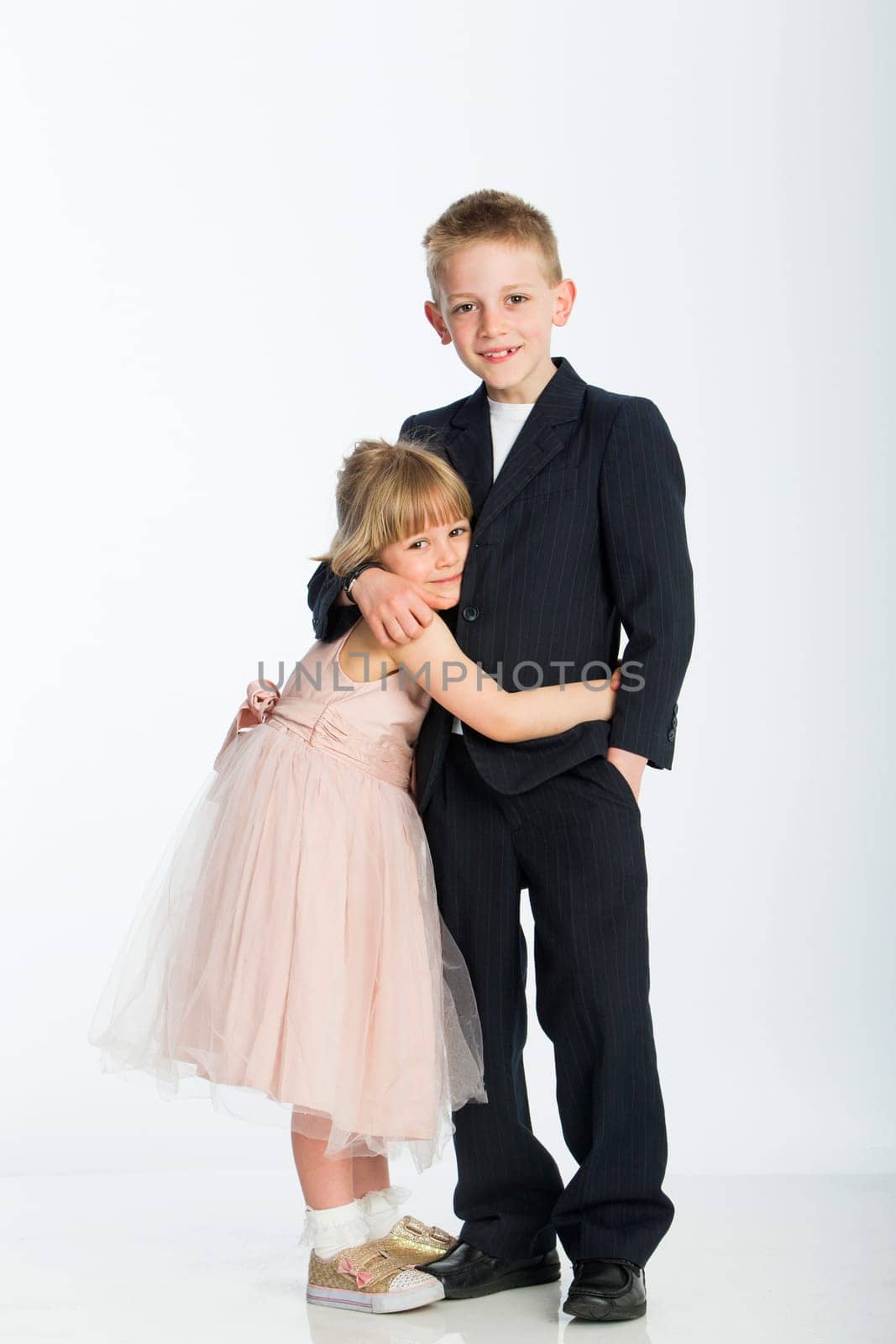 Formally dressed brother and sister. They are hugging and smiling for the camera against a white background
