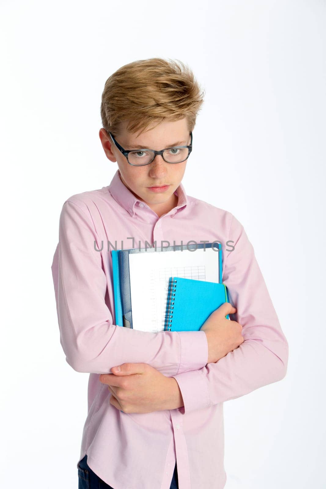 Young boy looking worried with his school folders in his arms. He is standing against a white background.