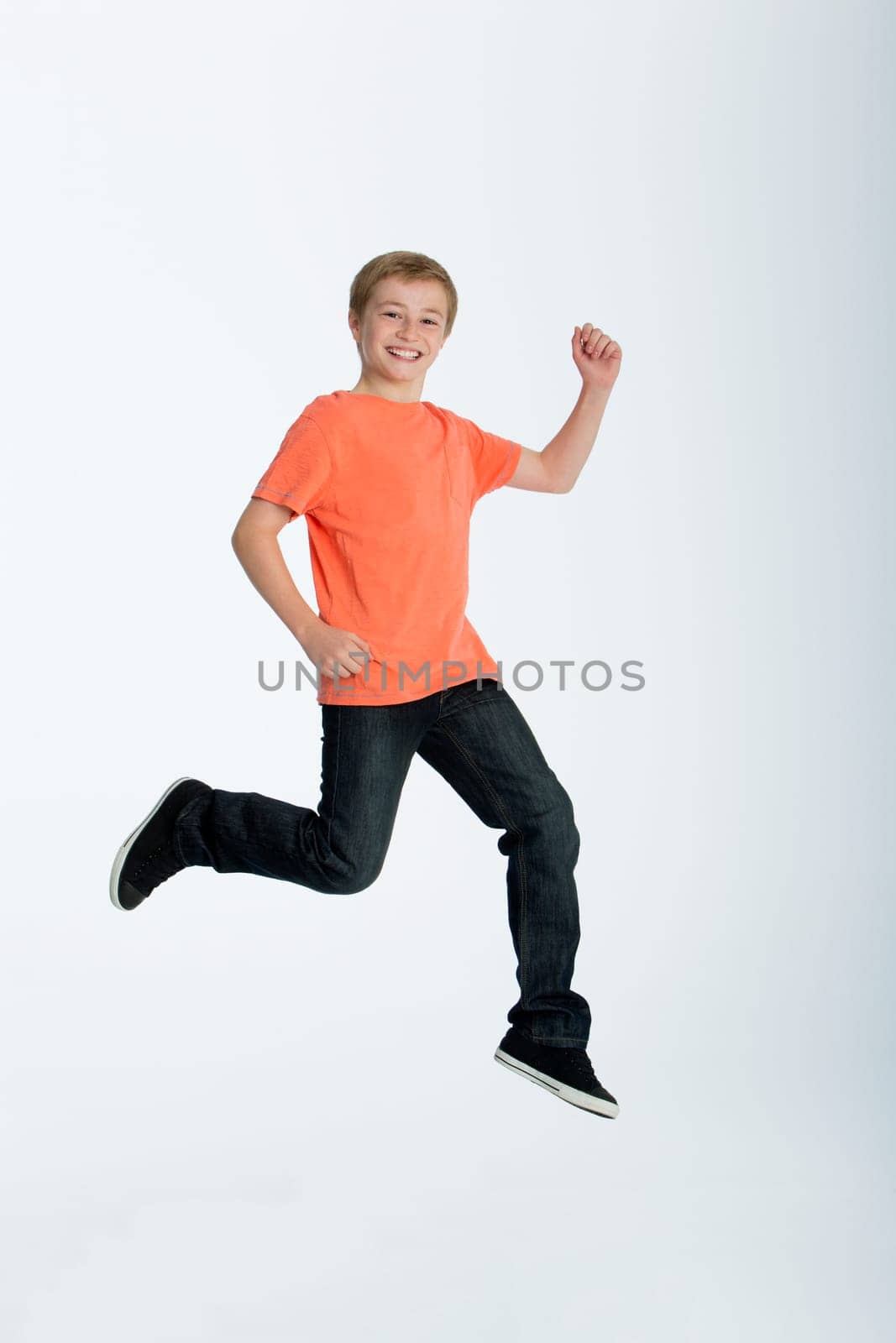 Young boy striking a pose whilst jumping for the camera. He is against a white background and is smiling.