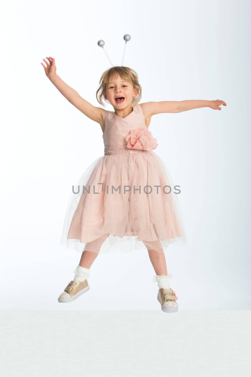 Cute little girl wearing a dress and bumble bee boppers posing in mid air against a white background