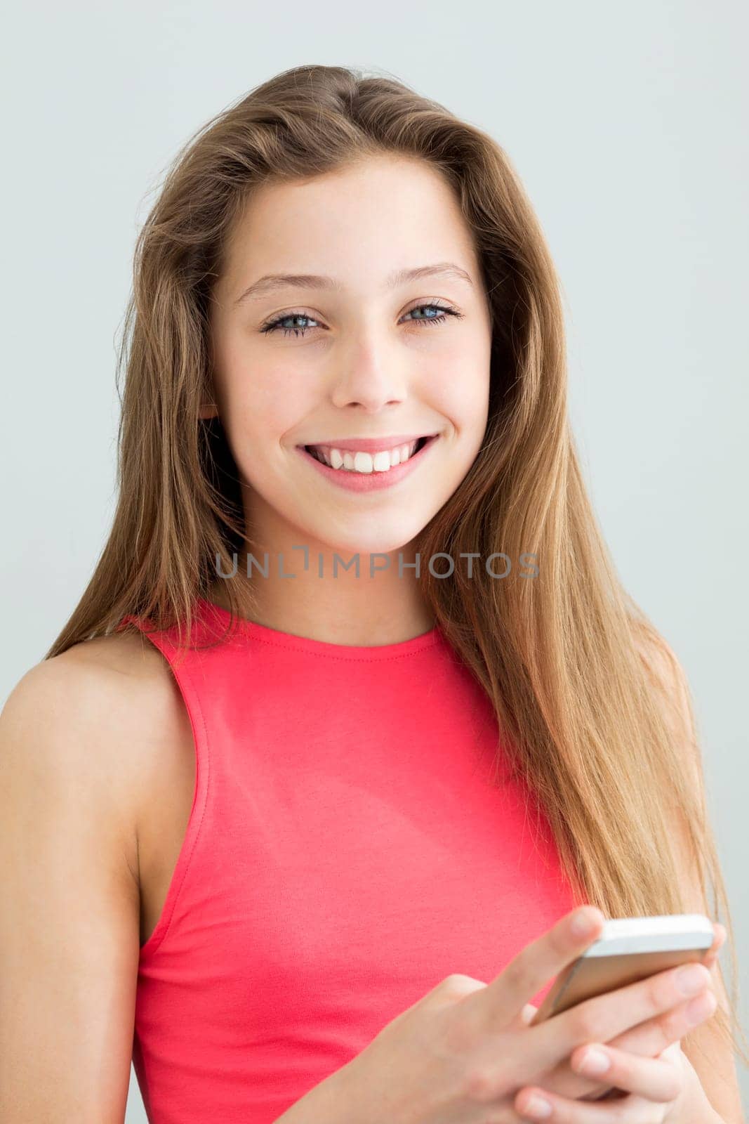Portrait of a teenage girl using a smartphone. She is smiling at the camera against a plain background.
