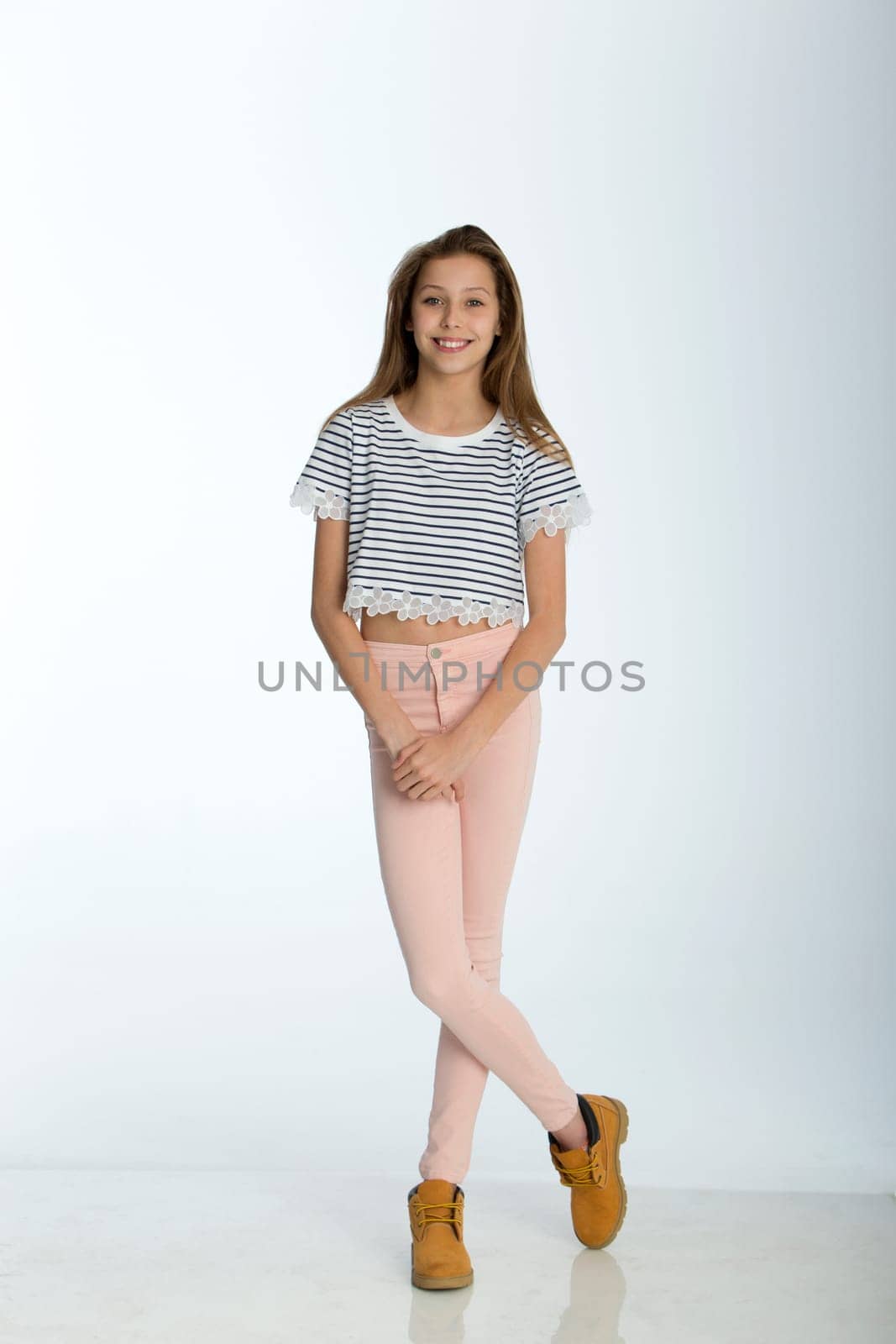 Full length portrait of a young girl against a white background. She is smiling for the camera.