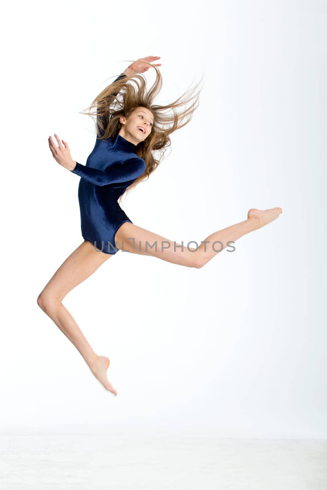 Gymnast posing in mid air against a white background. She is wearing a blue leotard.