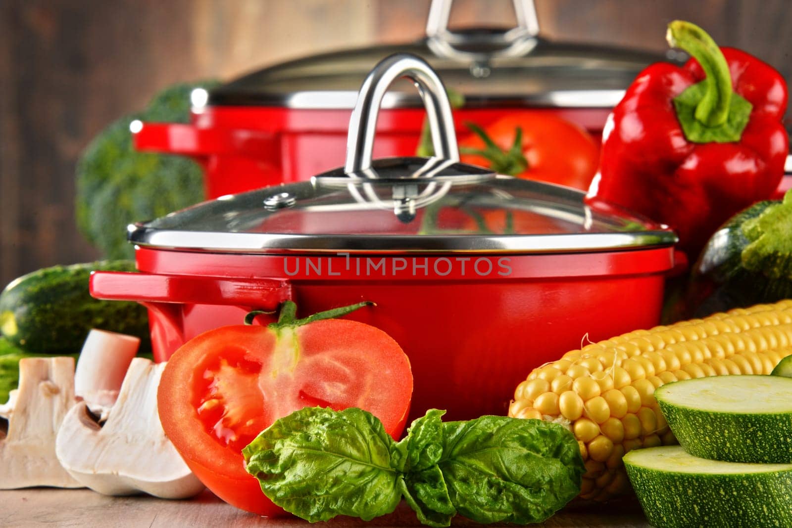 Composition with red steel pots and variety of fresh vegetables.
