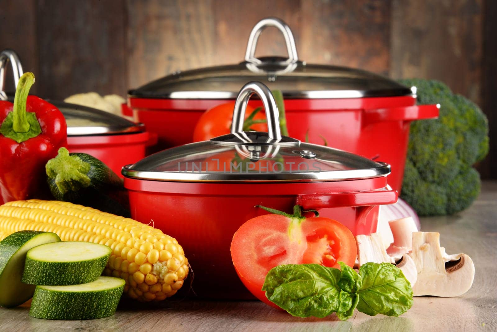 Composition with red steel pots and variety of fresh vegetables.