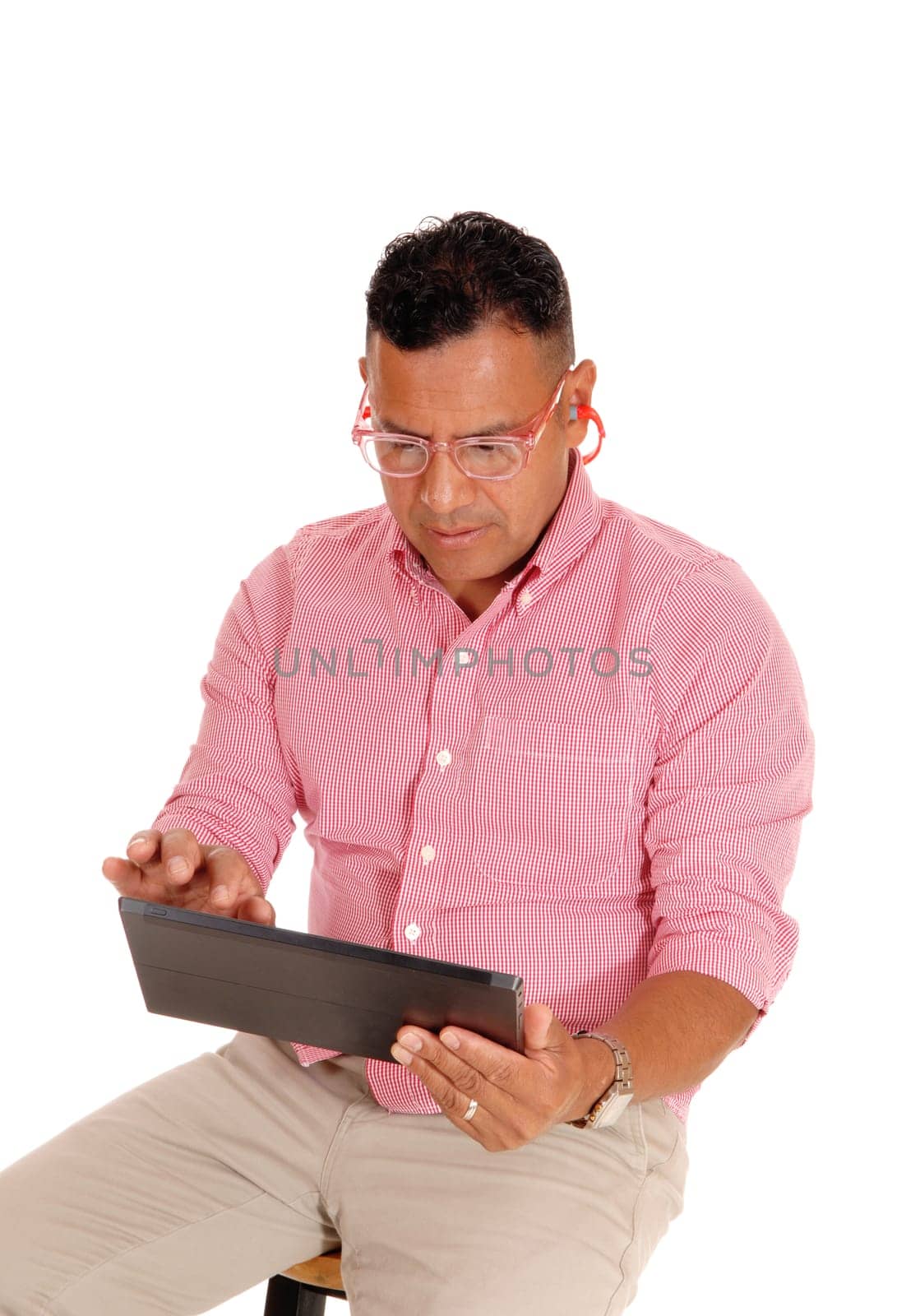 A middle age Hispanic man sitting on a chair, working on his tablet .computer, with safety glasses and earplug's, isolated for white background..