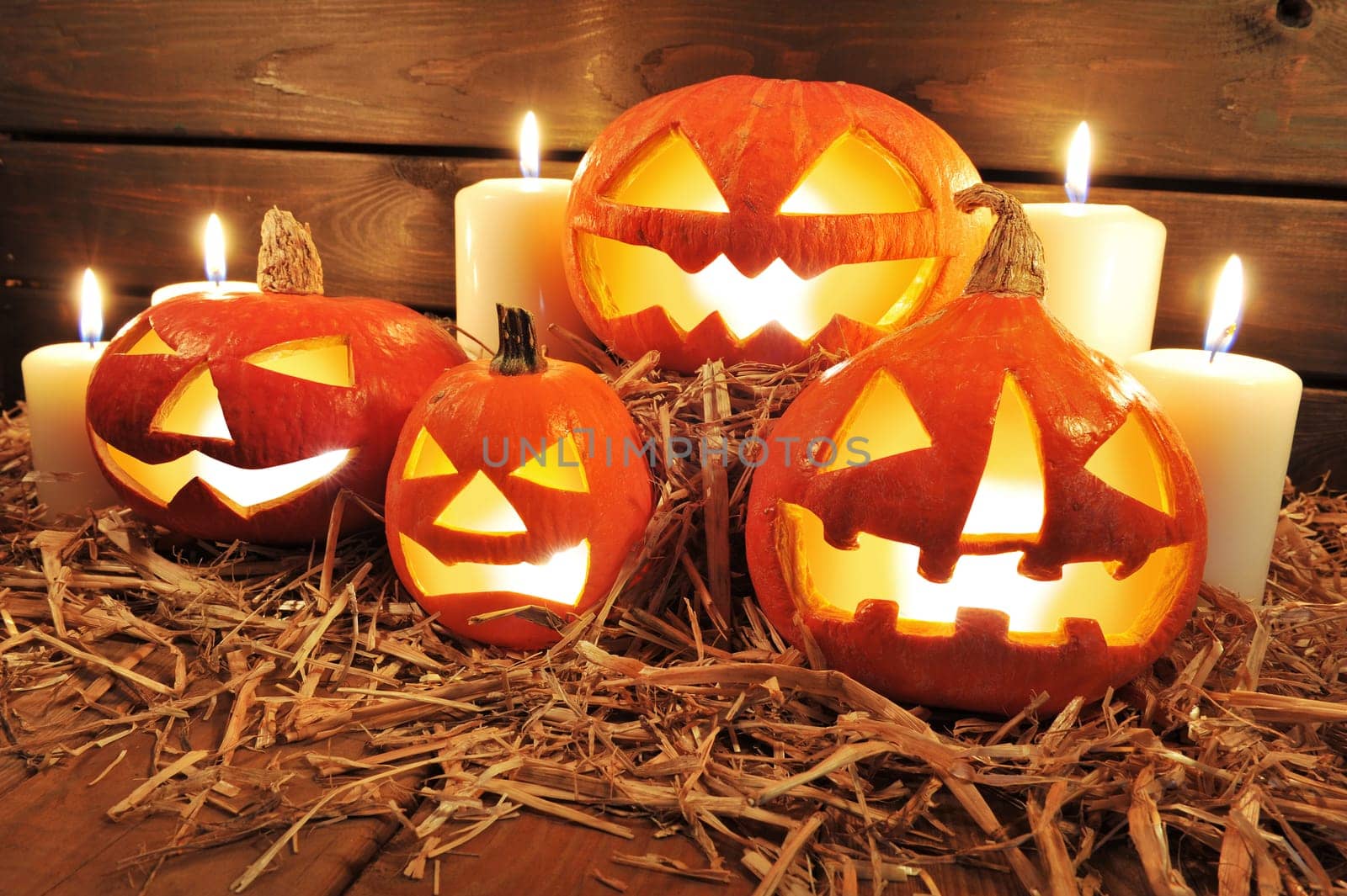 Three illuminated Halloween pumpkins with straw on old weathered wooden boards against a red-brown background in red light