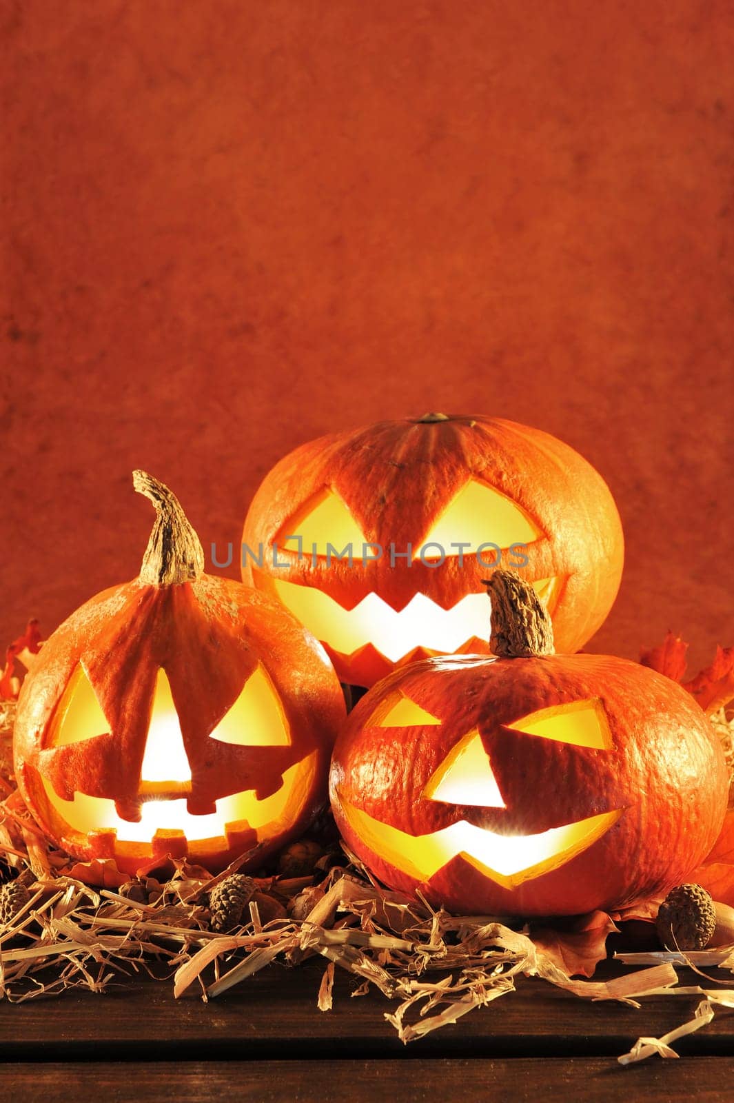 Three red illuminated Halloween pumpkins with straw on old weathered wooden boards against a brown background