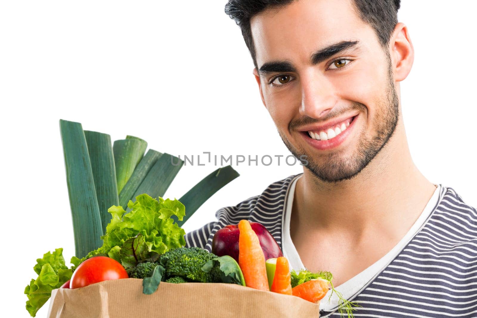 Handsome young man carrying a bag full of vegetables, isolated over white background
