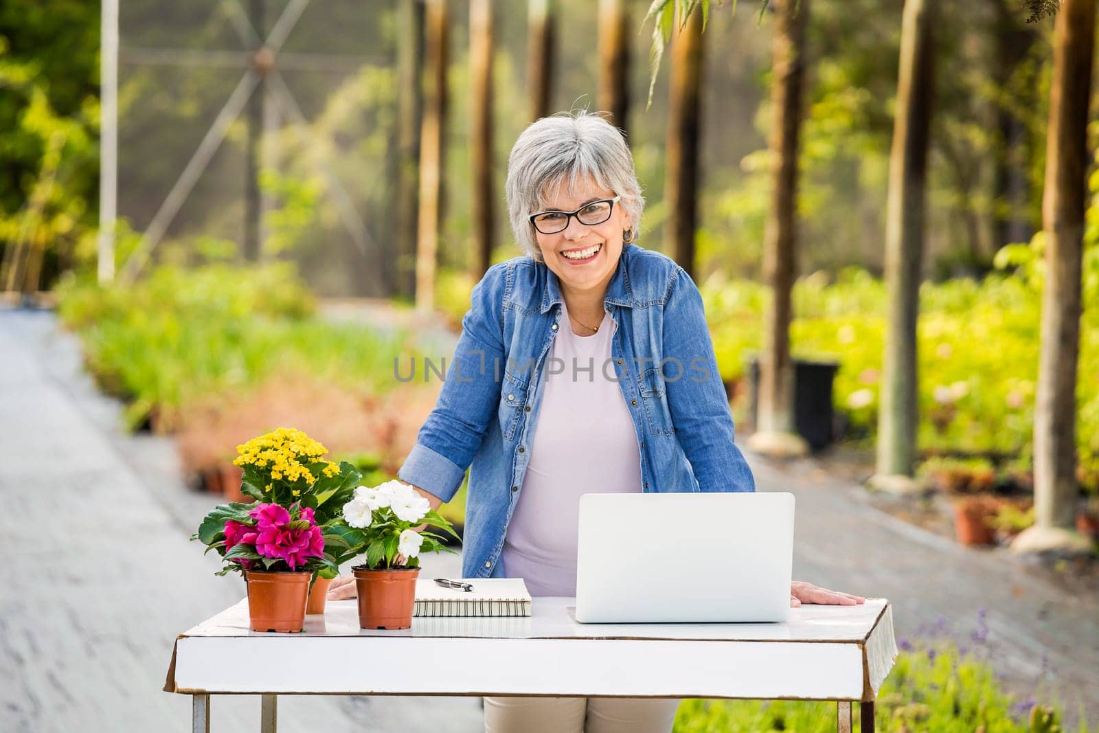 Beautiful mature woman working in a greenhouse holding flowers on her hands