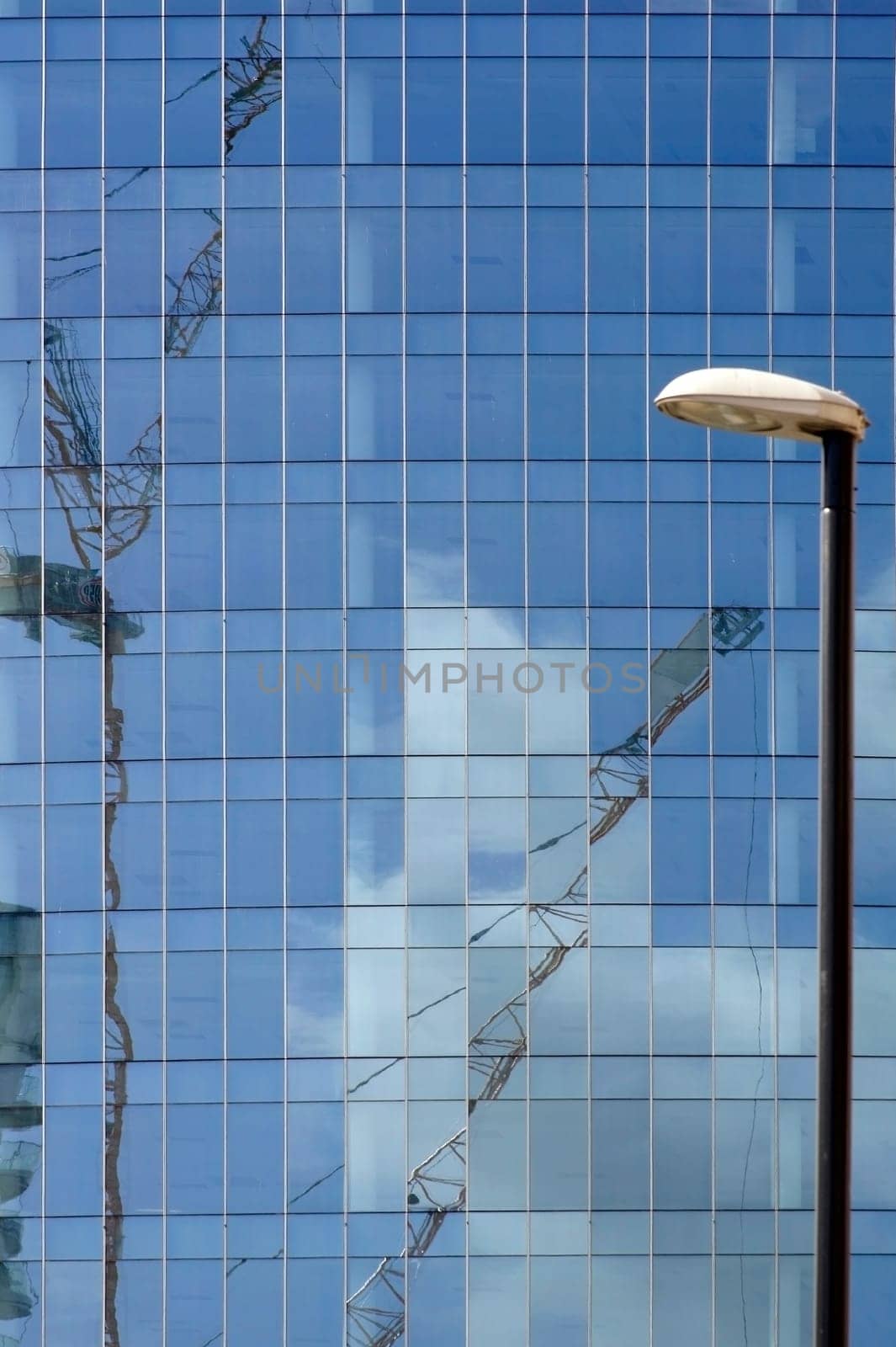 The facade of a modern office building with reflections of clouds and a crane in the windows.