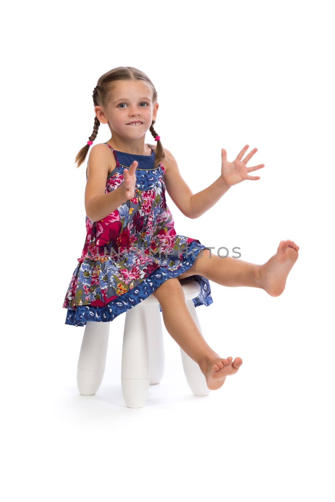 Little girl in a colored dress on a chair in the studio, isolate on white.