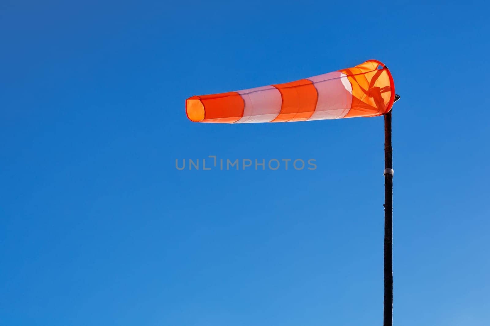 Orange and white windsock blows against a blue sky.
