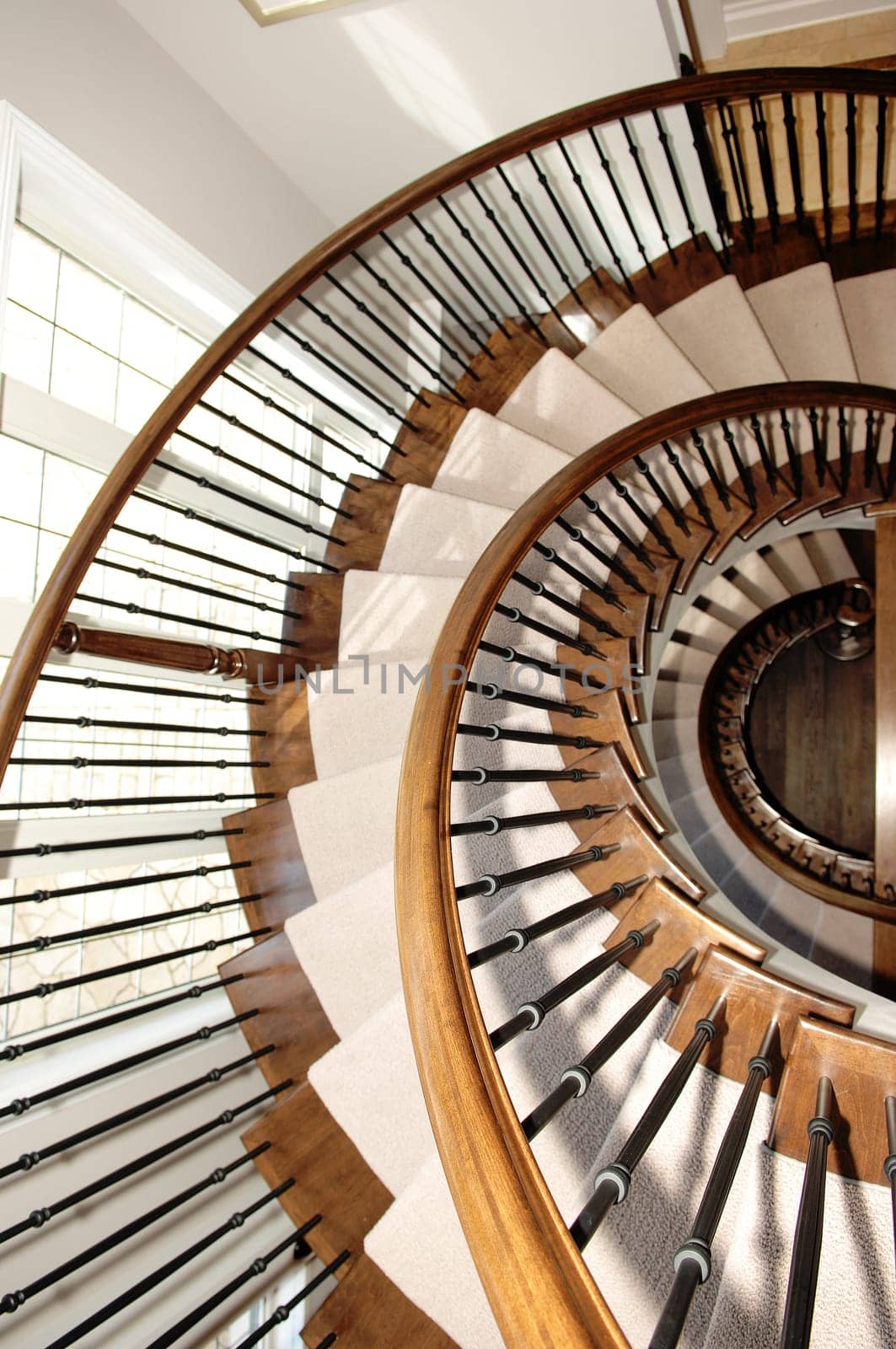 A beautiful round staircase in a closeup picture over three floors in oak.wood whit carpet and a window on the left..