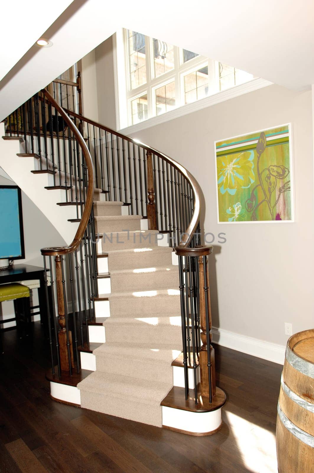 A round staircase to the basement bar in a new house with hardwood.floor and a beer barrel in the foreground..