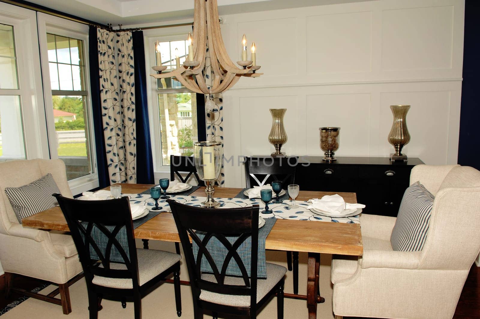 A modern living room in a new house with a table and chairs and two.windows and a light fixture..