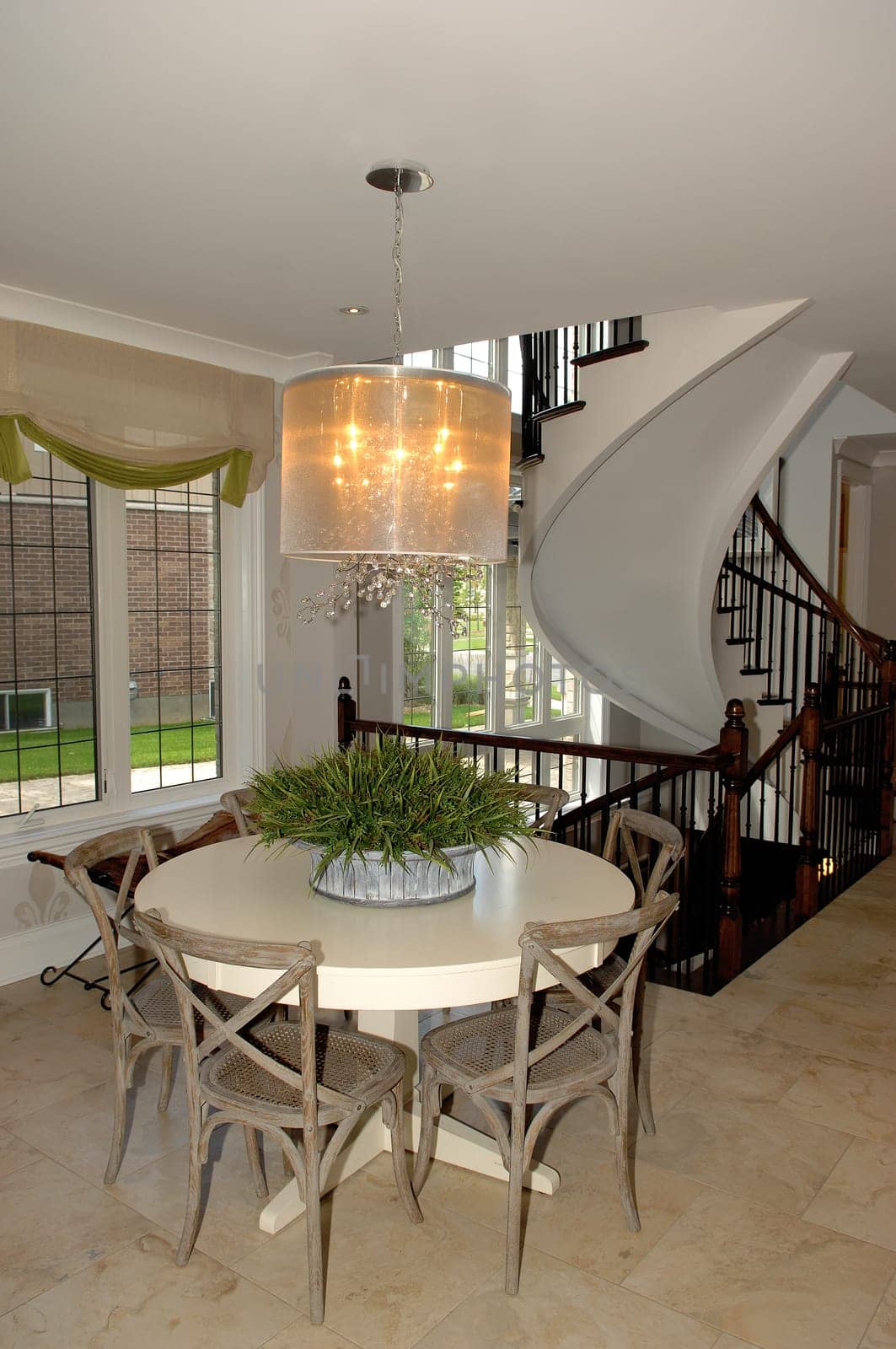 A beautiful dining area in a new house with a table and four chairs, .light fixture and a round staircase in the back..
