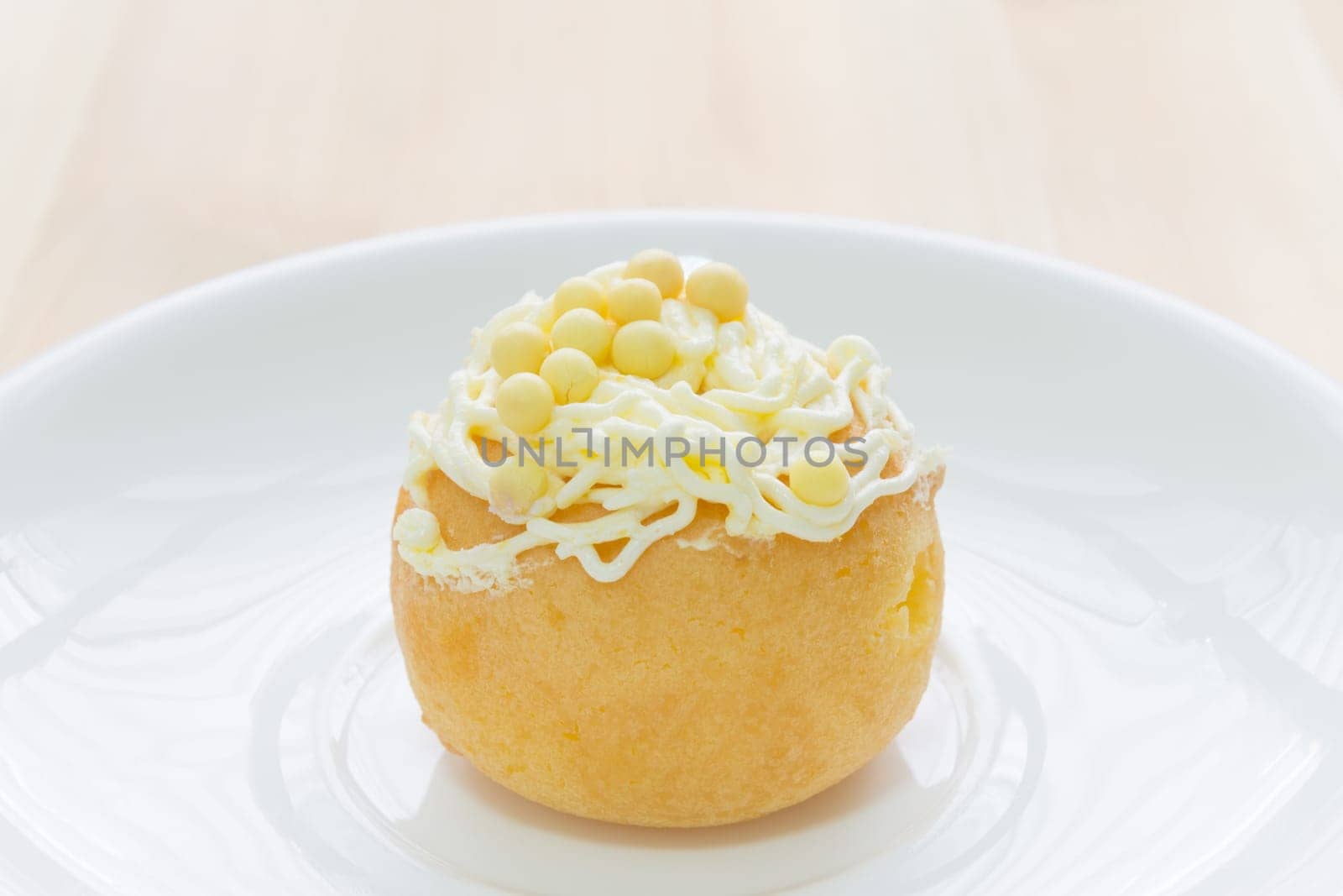 Yellow choux pastry or cream puff or profiterole that have whipped cream on the head. Eclair dessert on wood table.