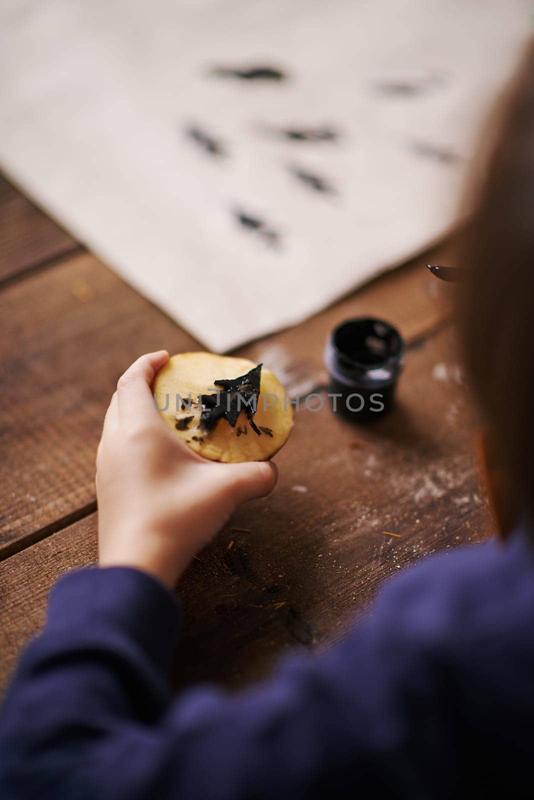 Hand of a child holding potato half with black firtree shape painted by gouache