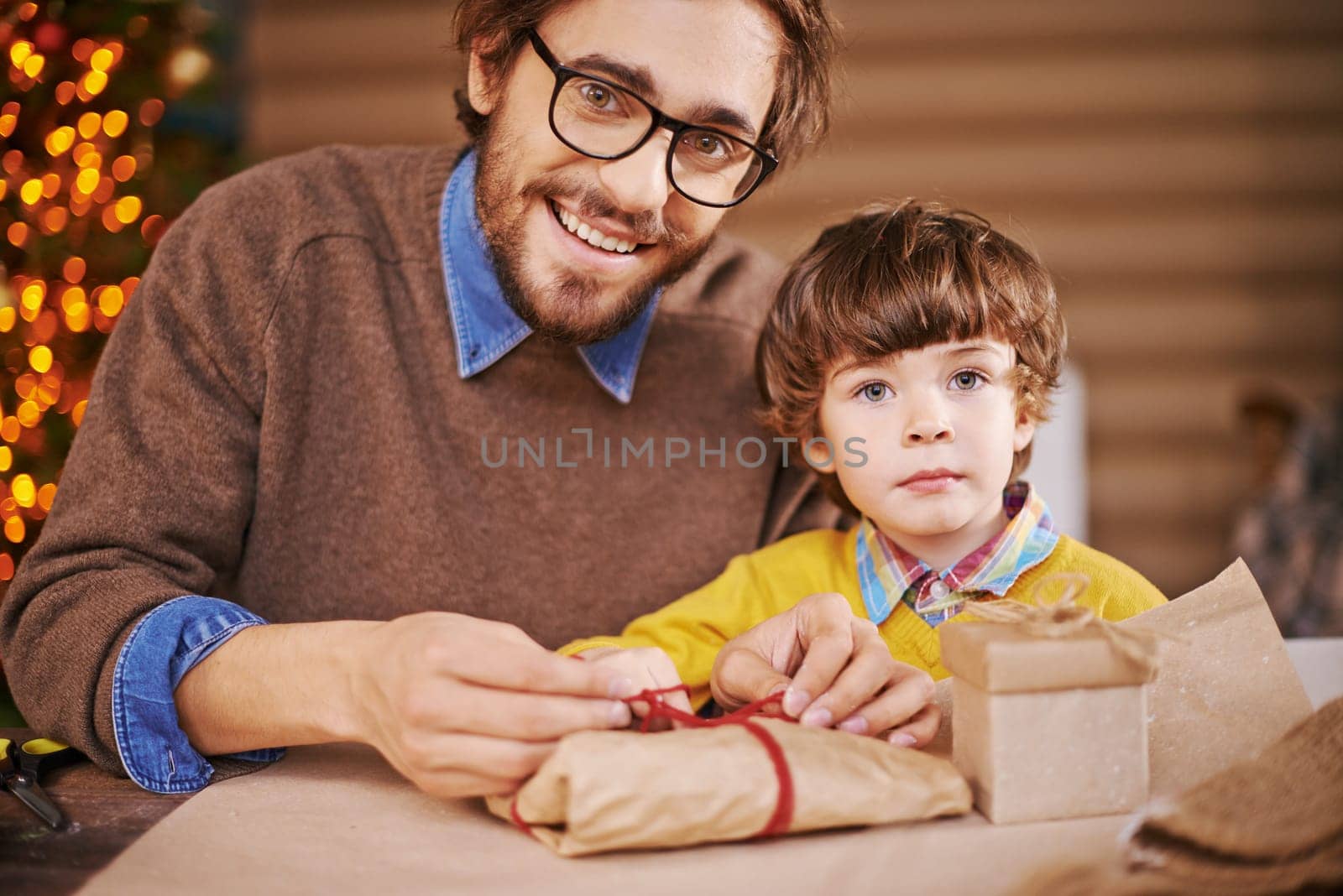 Young man packing xmas gift and looking at camera with his son near by