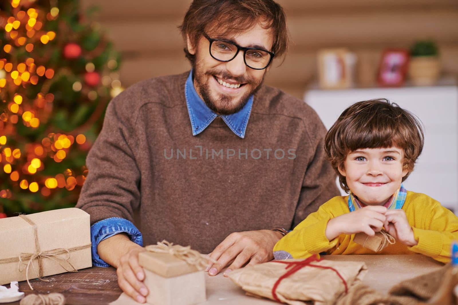Happy young man and his son looking at camera with packed xmas gifts near by