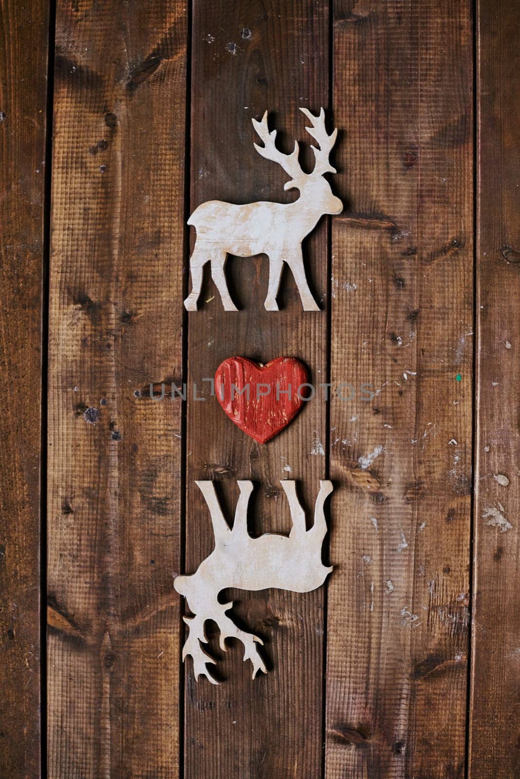 Two reindeers with red heart between them on wooden background
