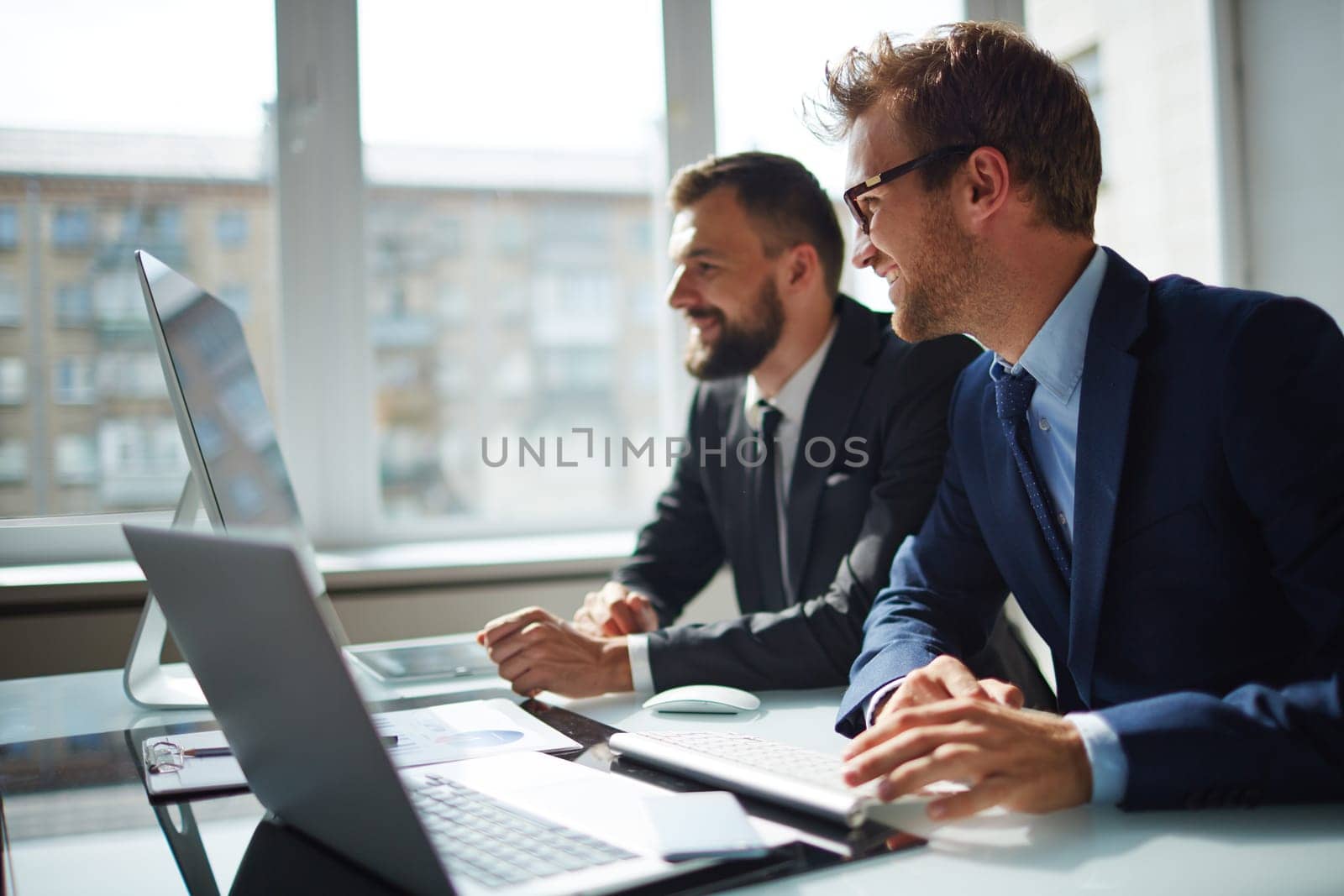 Smiling businessman and his colleague looking at computer monitor at meeting