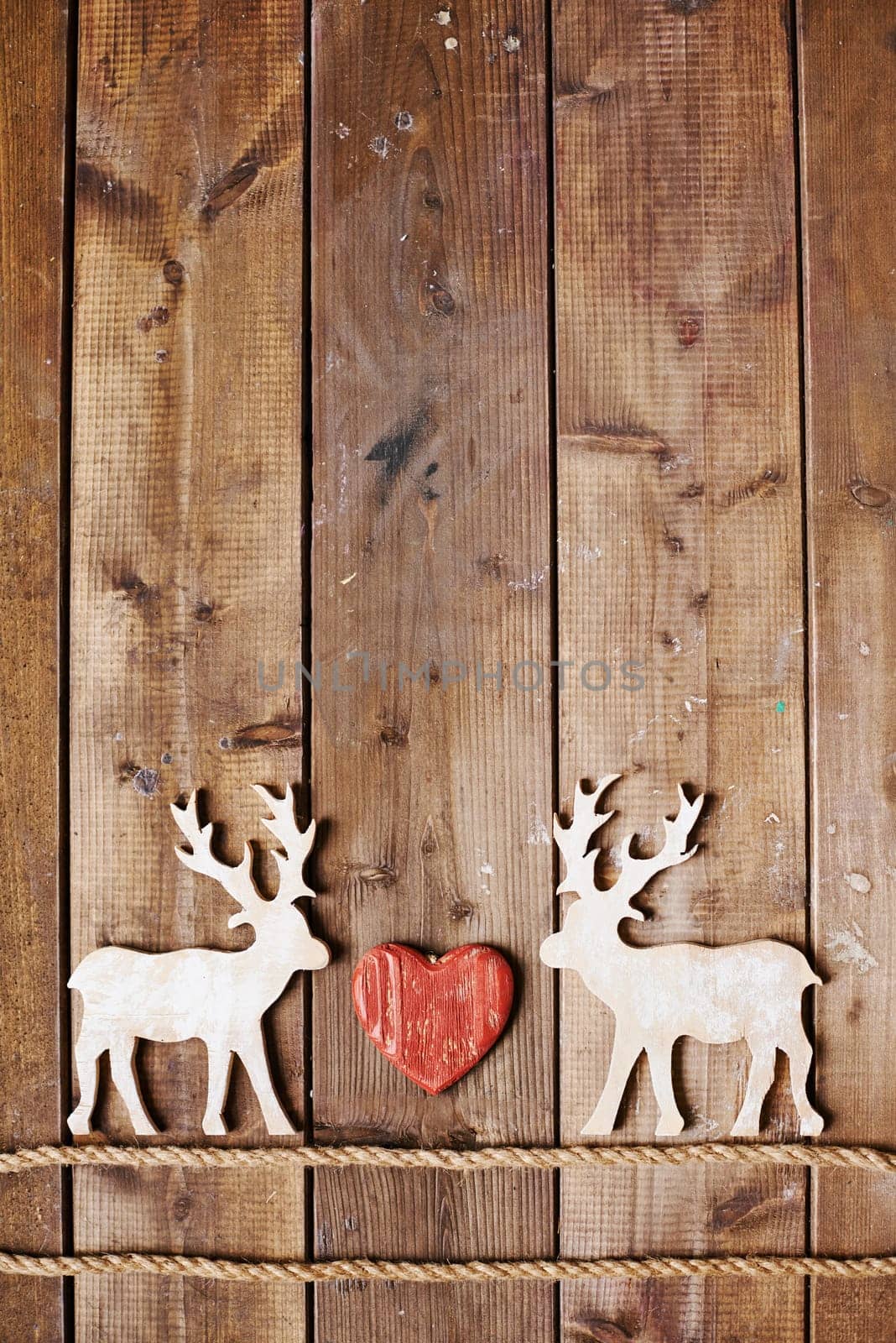 Two reindeers on ropes and red heart between them on wooden background