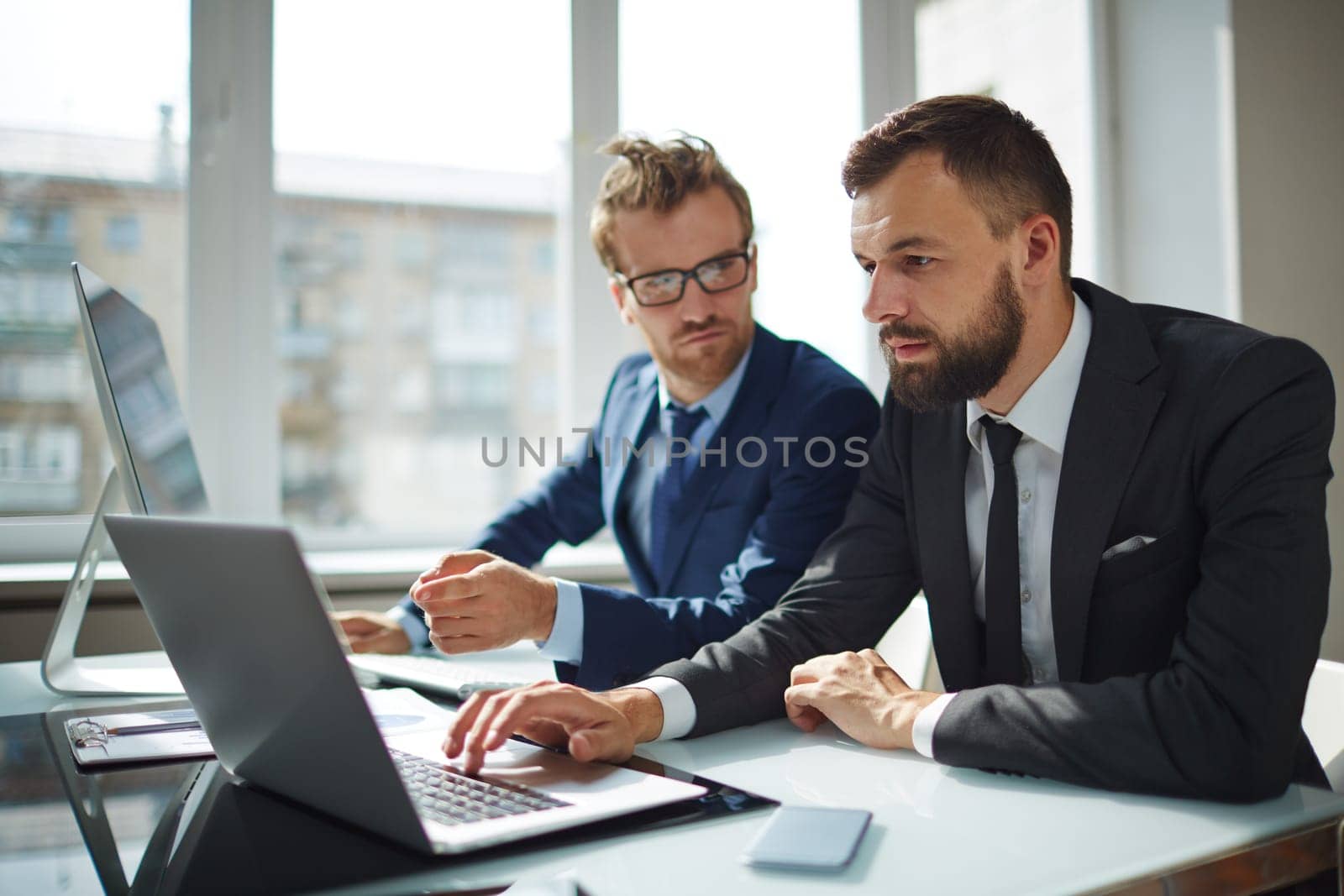 Serious employee browsing on laptop while his co-worker pointing at its display