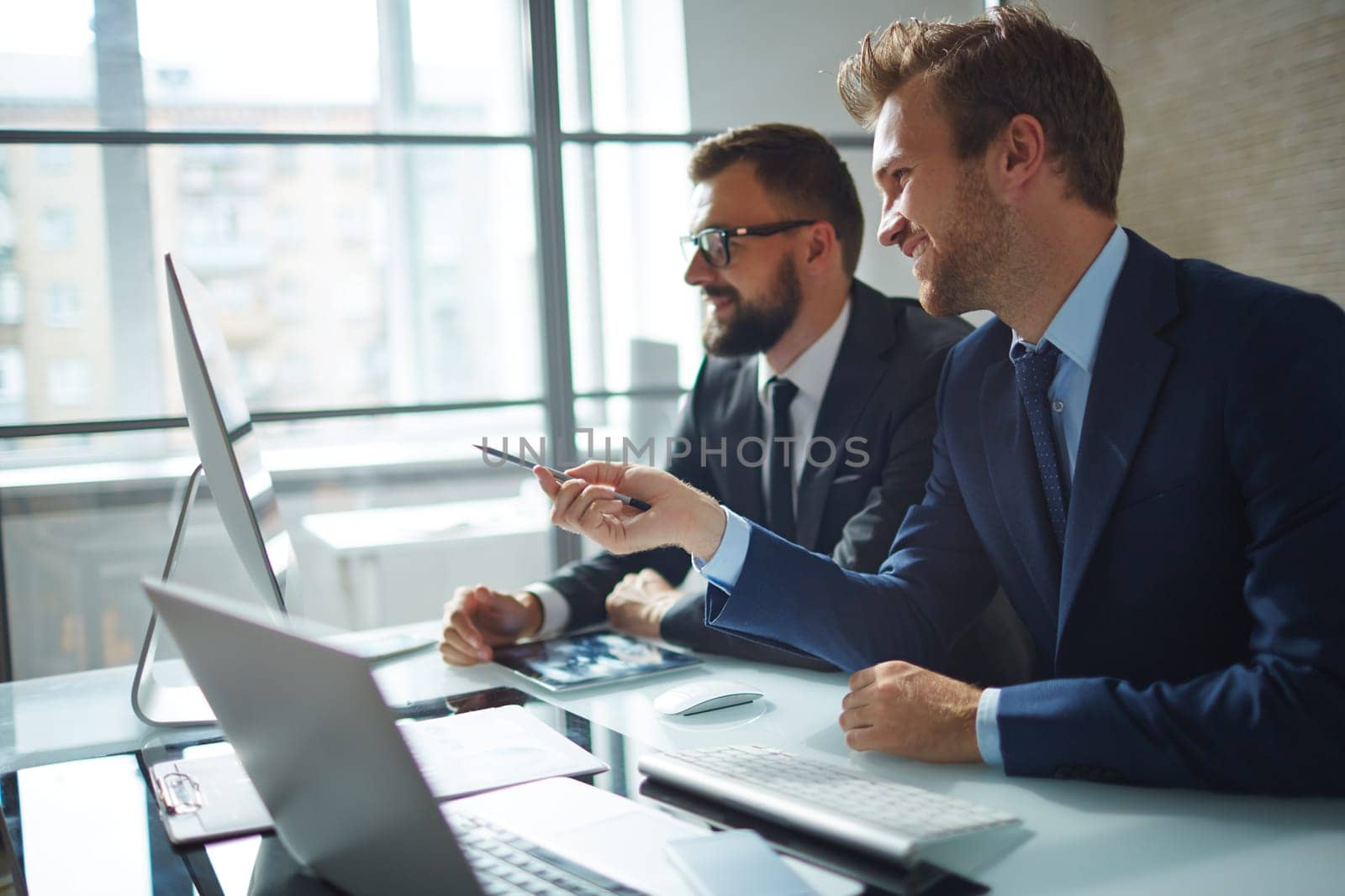Confident businessman consulting his colleague and pointing at computer monitor at meeting