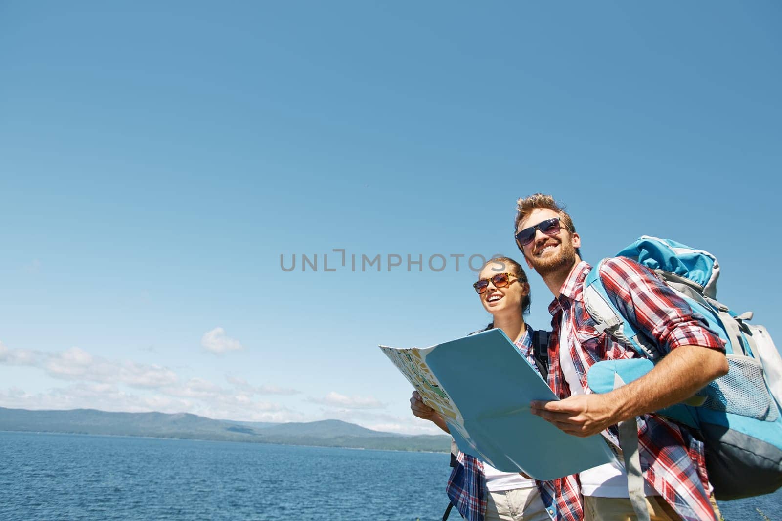 Cheerful hikers with map enjoying their trip on background of sky and sea